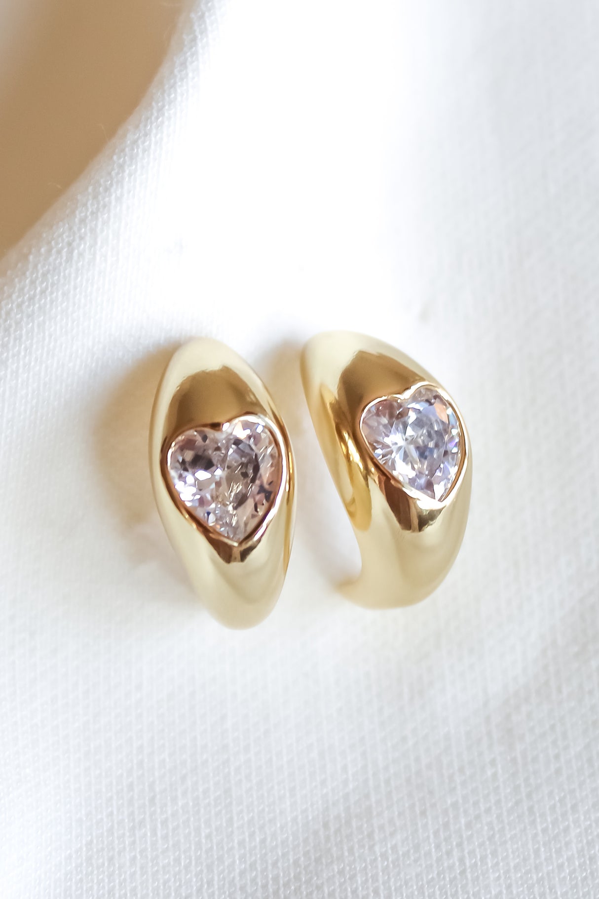 The Robbie Earring by Kinsey Designs Archives features teardrop-shaped clear gemstones on gold-filled settings, displayed on white fabric. Add elegance to any look—shop our sample sale now!.