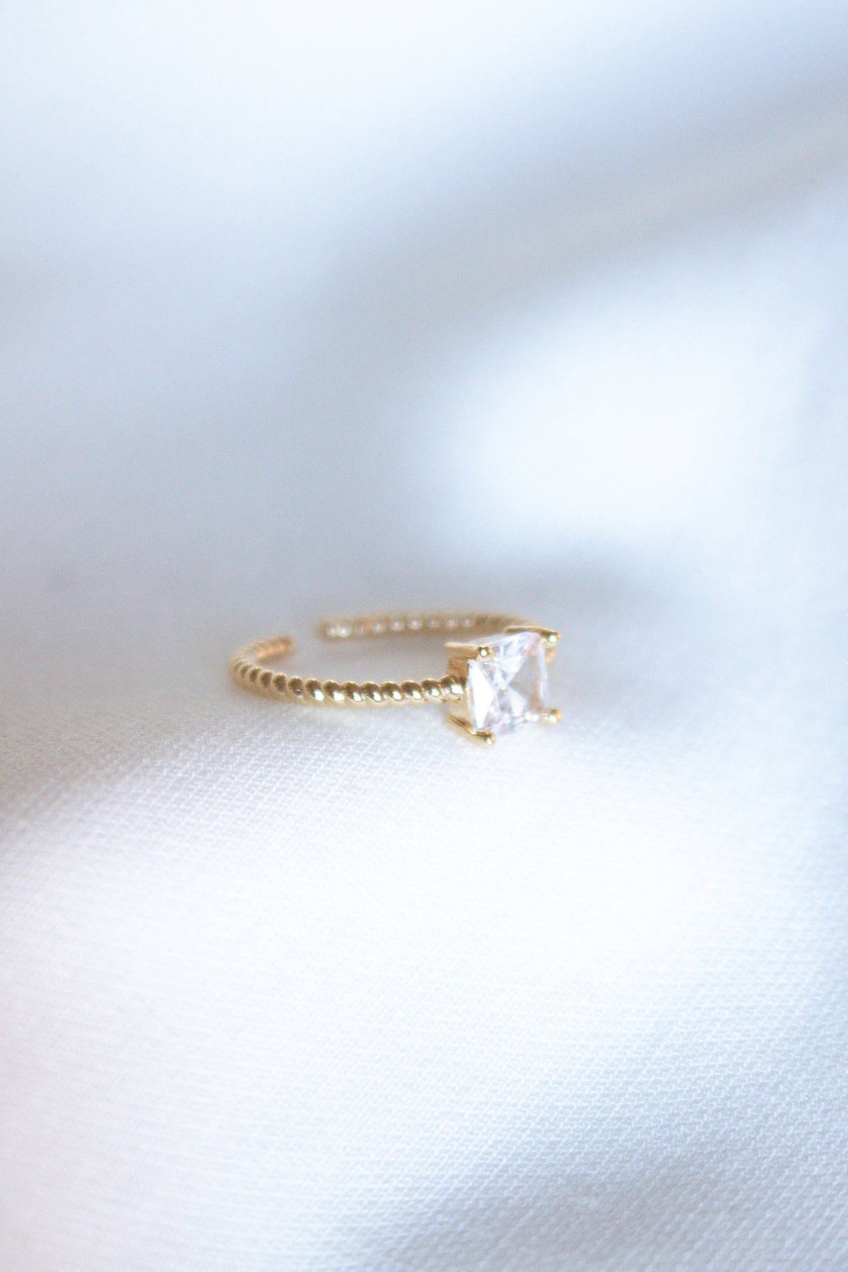 The Rose Ring - Sale by Kinsey Designs Archives features a delicate gold-filled band with a square-cut cubic zirconia, shown resting gently on soft white fabric.