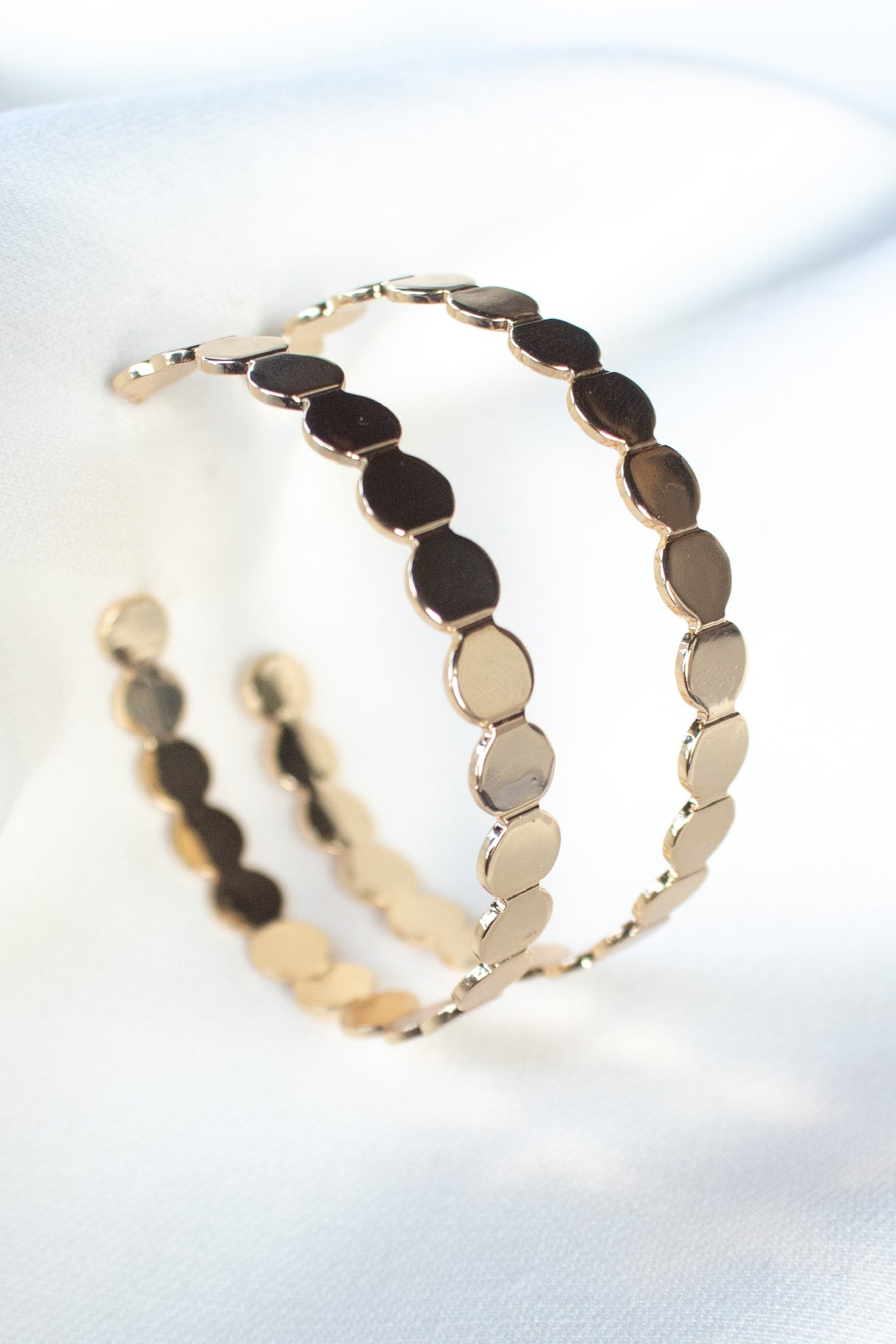 The Kinsey Designs Archives "Round and Round Hoop" earrings feature a scalloped, disc-like gold-filled design, measuring 2" wide and elegantly showcased on a soft white fabric background.