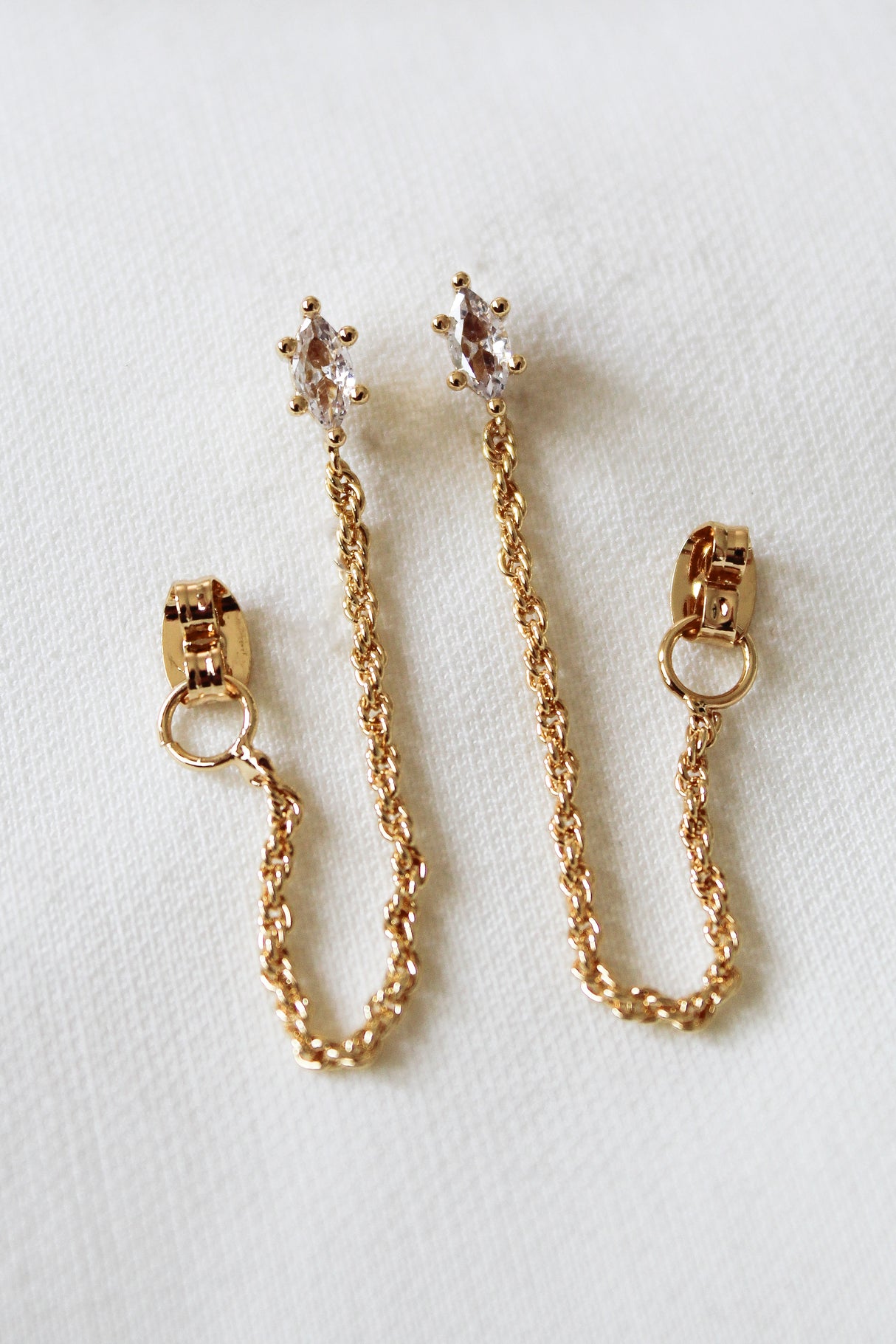 The Kinsey Designs Sadie Wrap Earrings are gold filled, 1.25" long, with clear gemstone studs, displayed on a white fabric background.