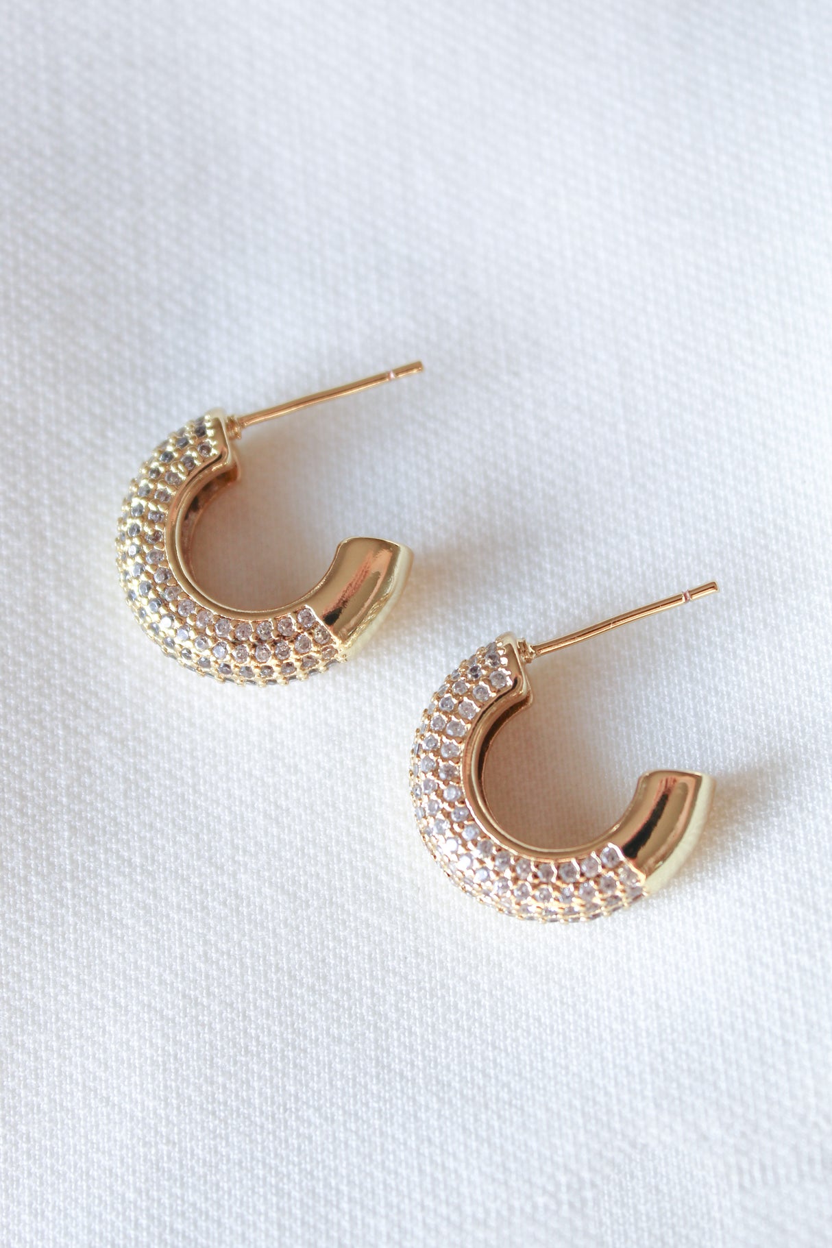 The Kinsey Designs Sax Hoop earrings are gold filled, feature small clear crystals, and measure 0.85" in diameter. Displayed on a white textured fabric background.