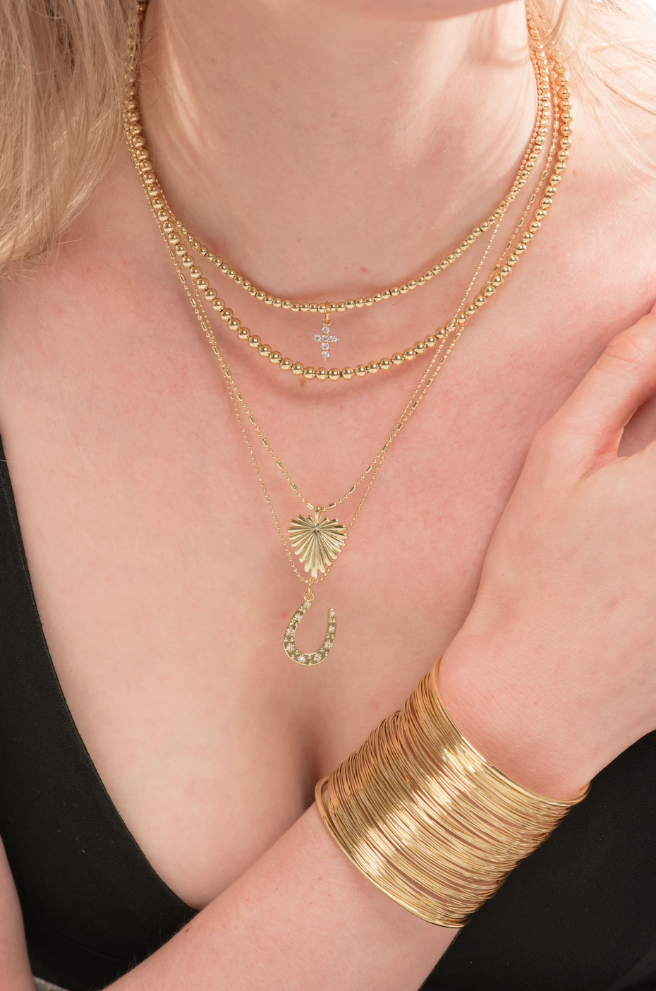 A woman wears Kinsey Designs' Lane Hoop layered gold necklaces and a wide gold bangle (.75" circumference), paired with a black V-neck top.