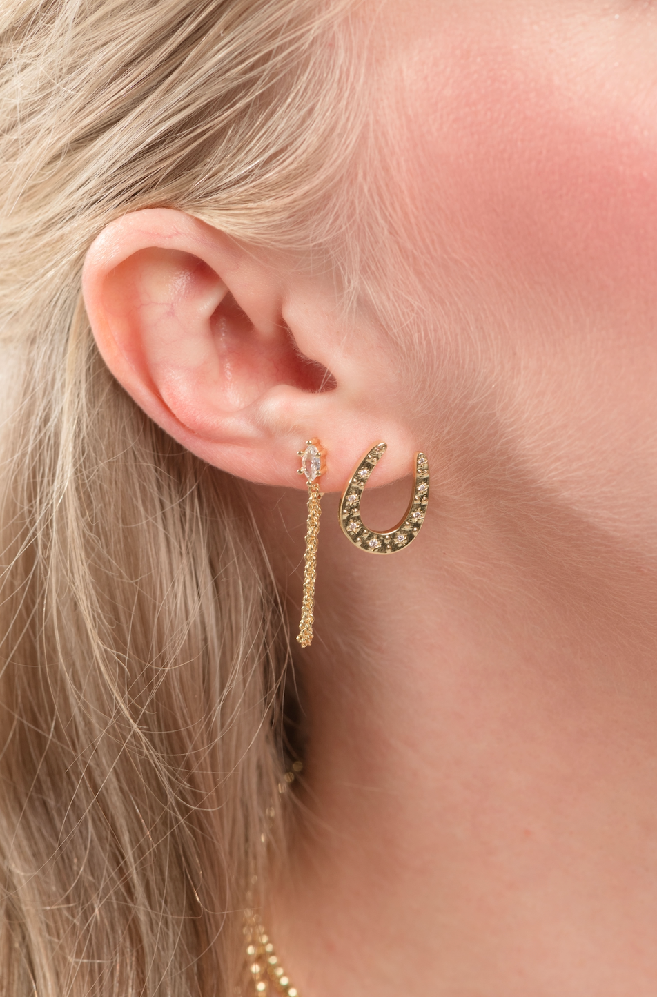 Close-up of a woman's ear wearing two Kinsey Designs Sadie Wrap Earrings—gold filled, one dangling at 1.25" and one horseshoe-shaped.