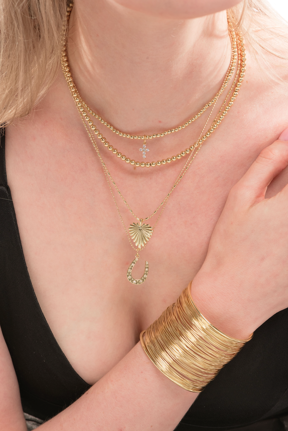 A woman in a black top wears the Kinsey Designs Selena Necklace, a layered gold charm necklace with 3mm beads, paired with a wide gold bangle.