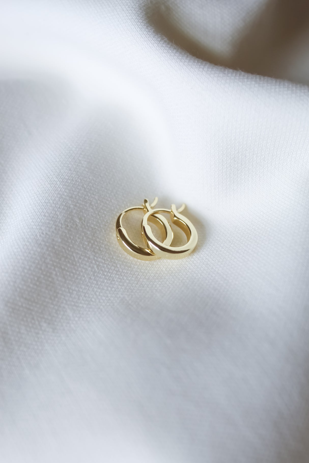 The Sleep-In Hoop earrings by Kinsey Designs are two small gold-filled hoops, each with a 0.5" diameter, displayed on soft white fabric.
