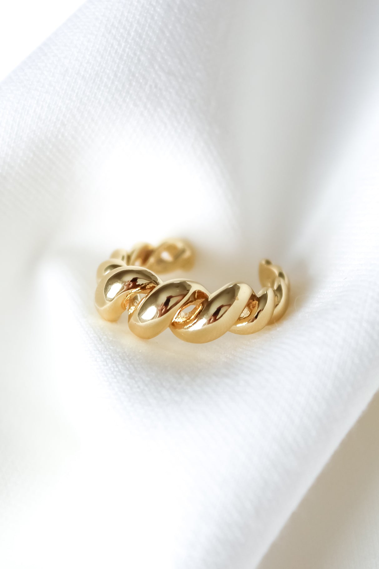 The Spyra Ring by Kinsey Designs, a gold filled chunky spiral ring, is displayed on soft white fabric under bright natural light.