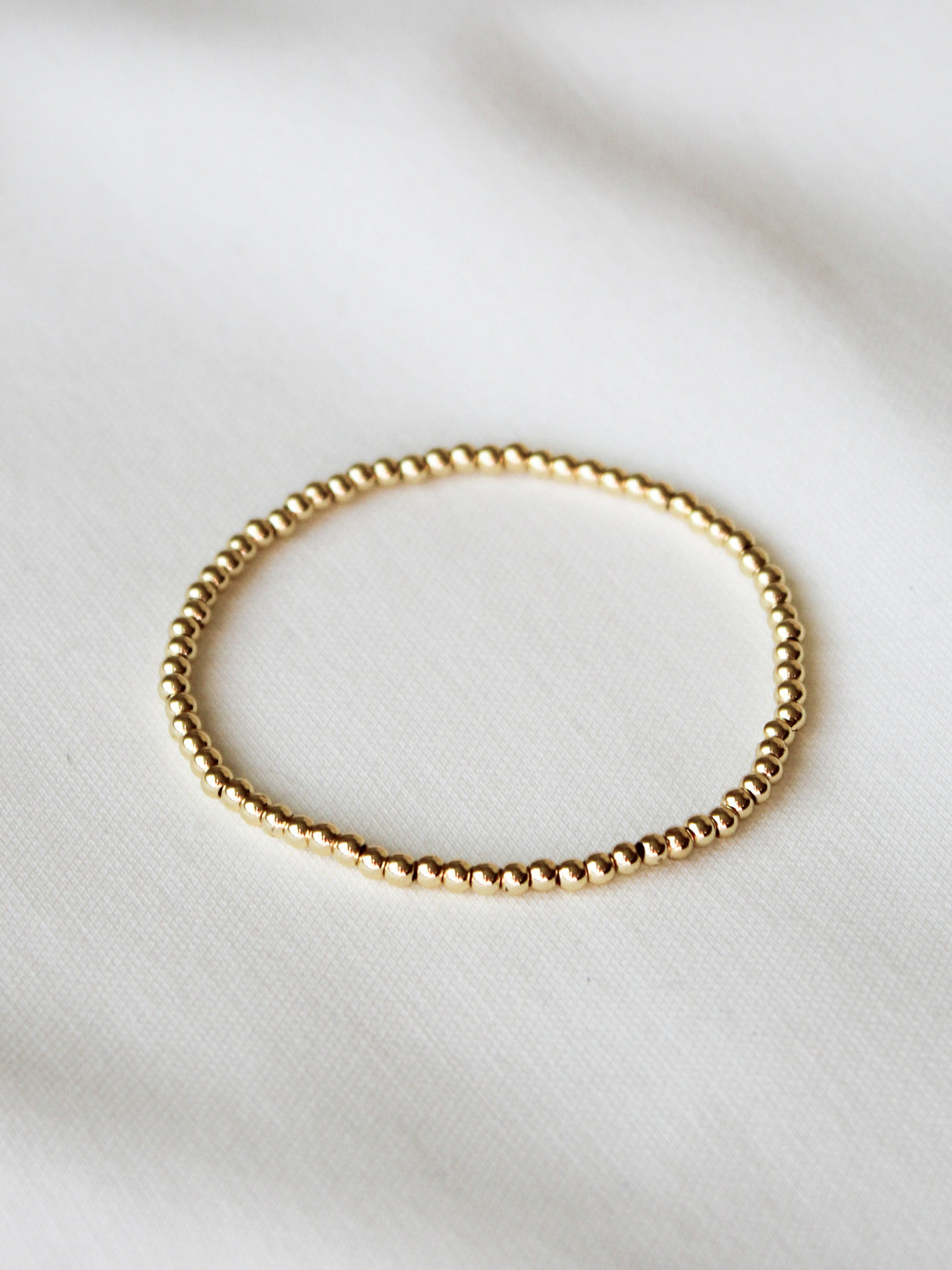The Kinsey Designs Stretch Bead Bracelet 3MM is a delicate gold filled bracelet displayed on soft white fabric, ideal for stacking or wearing alone.