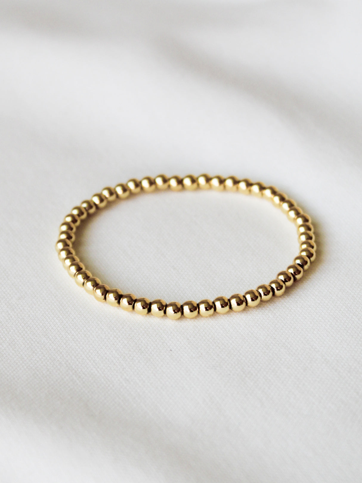 The Kinsey Designs Stretch Bead Bracelet 4MM rests on a white fabric background, perfect for stacking with your favorite styles.