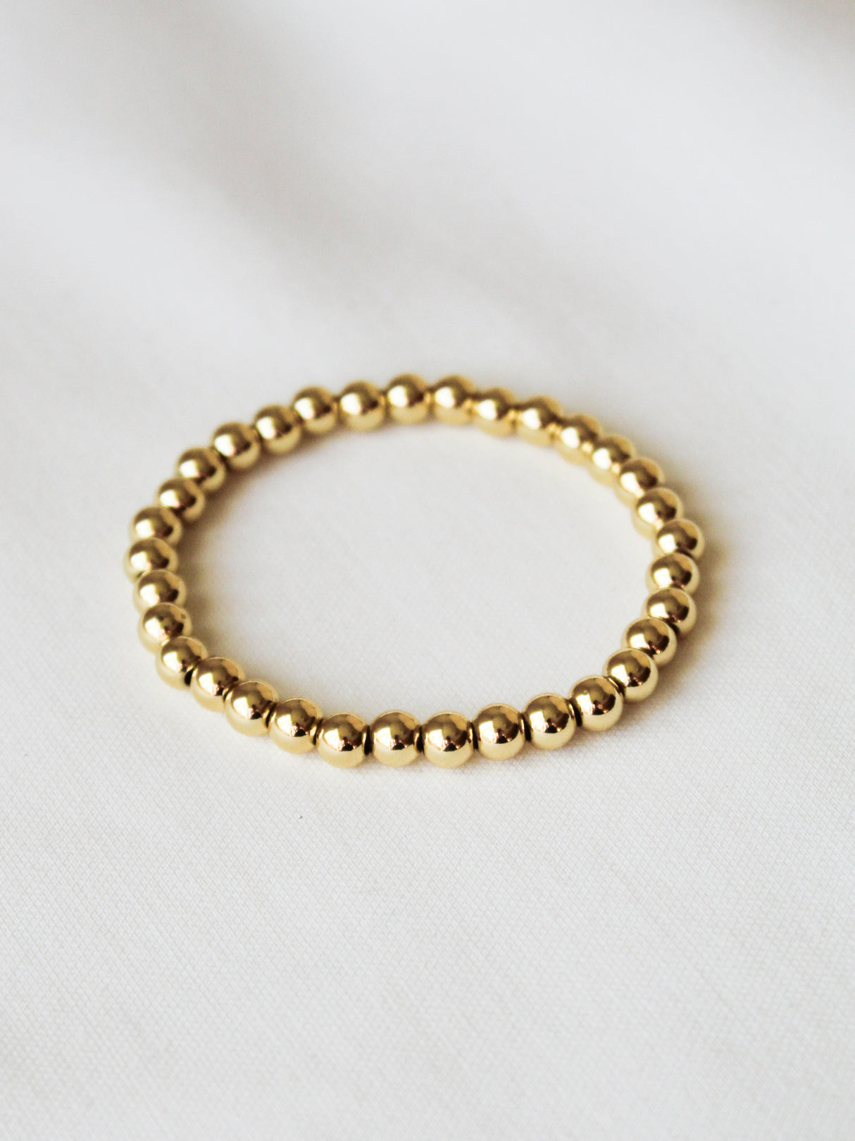 The Kinsey Designs Stretch Bead Bracelet 6MM is arranged in a circle on white fabric, highlighting its elegant beads and effortless style.