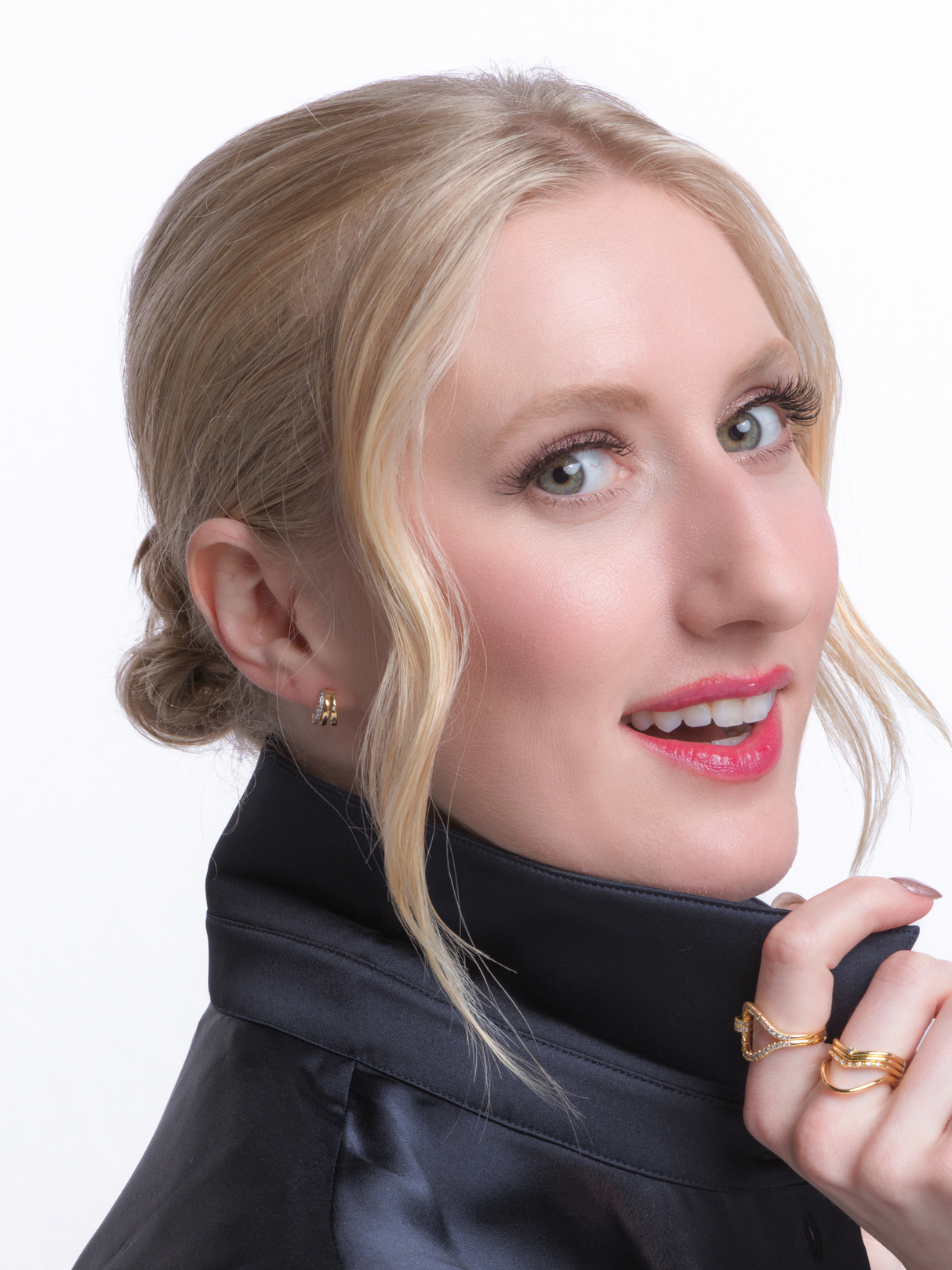 A blonde woman in a black jacket smiles, displaying red lipstick and gold Kinsey Designs Teddy Triple Earrings, set against a white background.