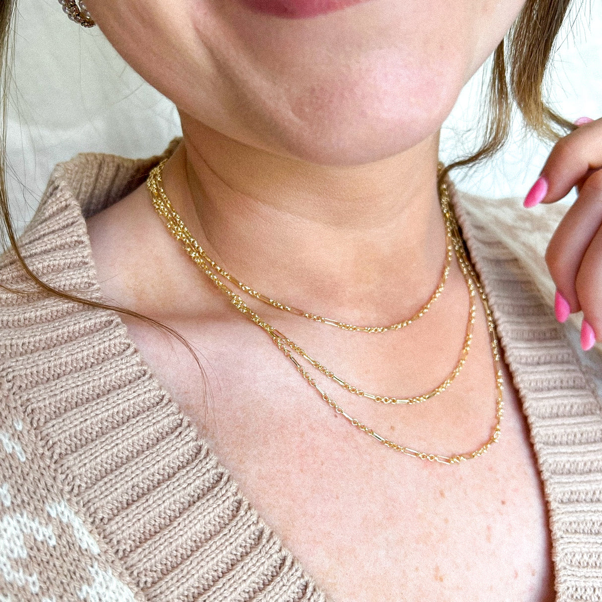 A smiling woman wearing the Tymes Necklace by Kinsey Designs and a beige knit sweater, with pink nail polish—an elegant touch for your next sample sale find.