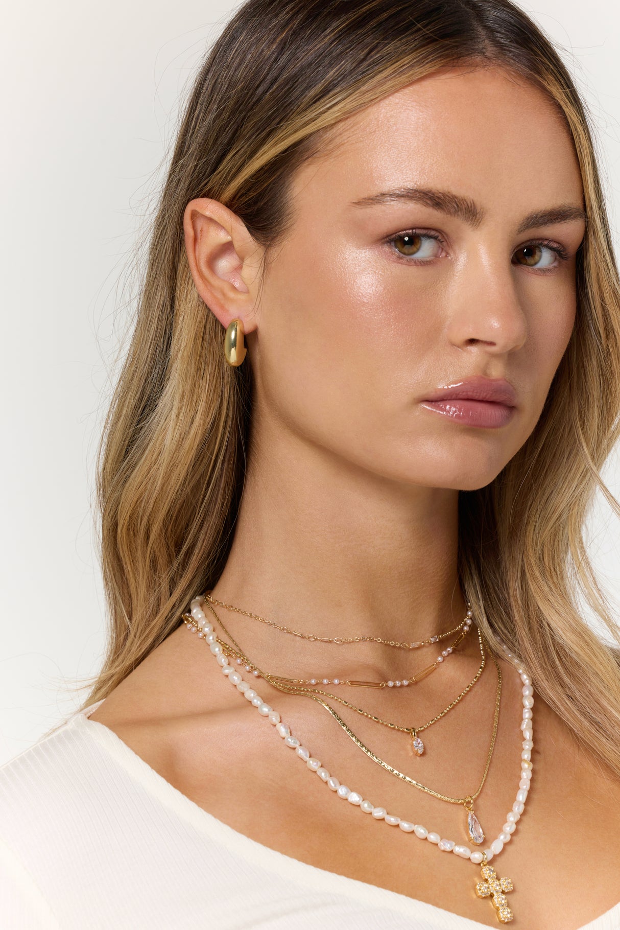 Woman with long blonde hair wearing Kinsey Designs’ Weston Earring, layered gold and pearl necklaces, a gold hoop earring, and a white top—perfect for your next sample sale find.