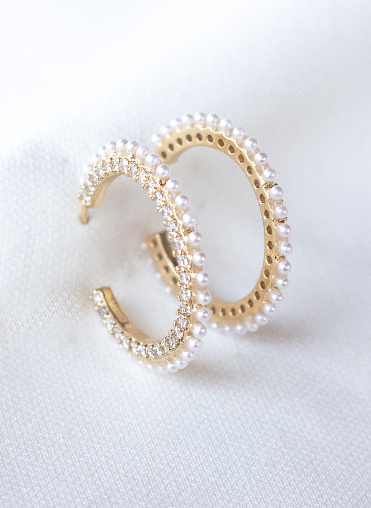 The Whit Hoop by Kinsey Designs Archives features gold-filled hoops adorned with small pearls and sparkling cubic zirconia, displayed on a white fabric background.
