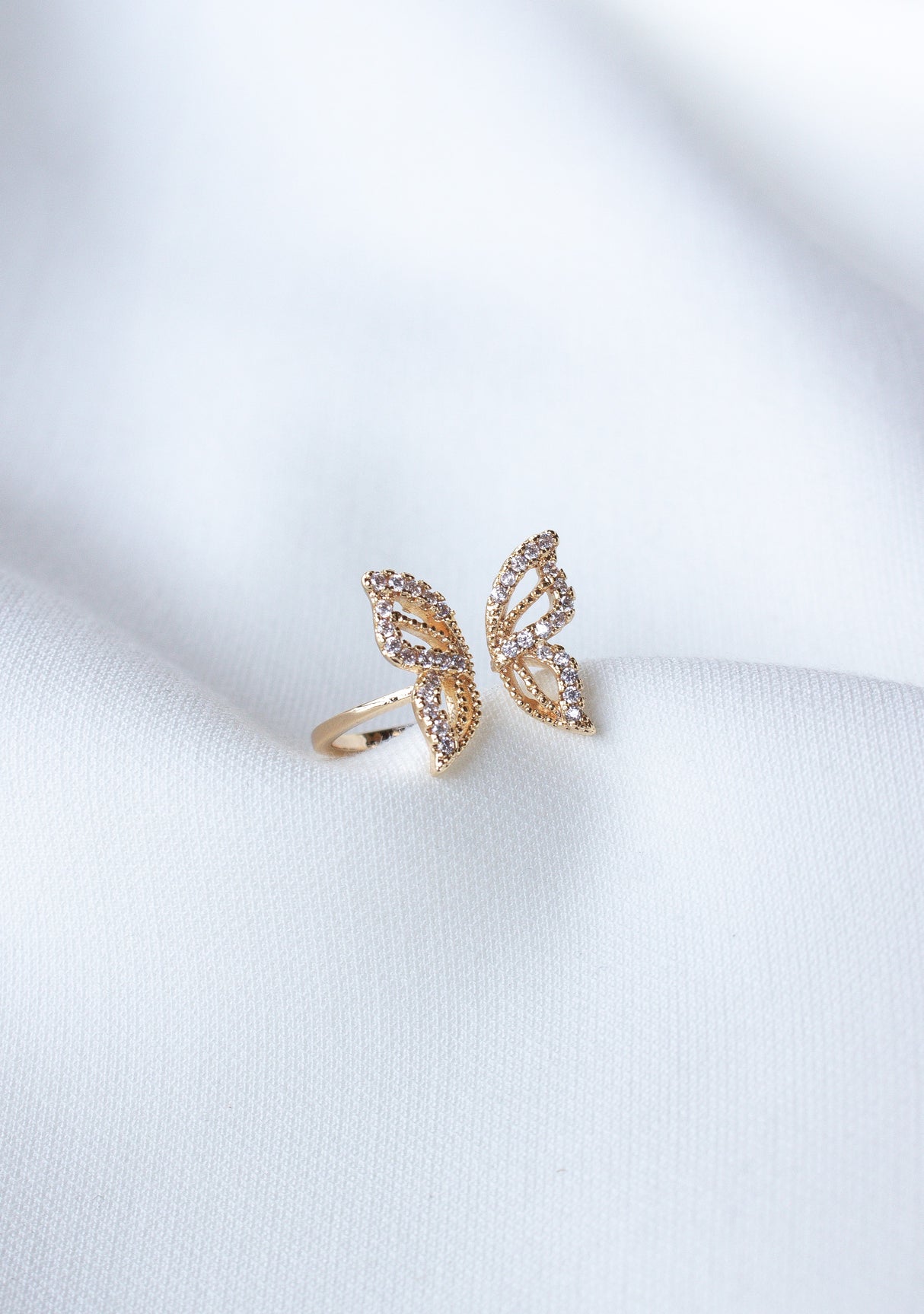 The Willow Butterfly Ring by Kinsey Designs Archives is a delicate gold-filled ring with a butterfly shape and small gemstones, elegantly shown on white fabric—ideal for butterfly jewelry lovers.