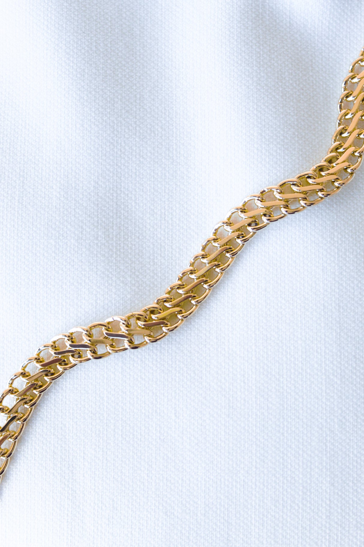 The Kinsey Designs Archives Woven Bracelet features interlocking gold filled links, displayed diagonally on white textured fabric—ideal as a 6-inch chain or a stylish chain extender.