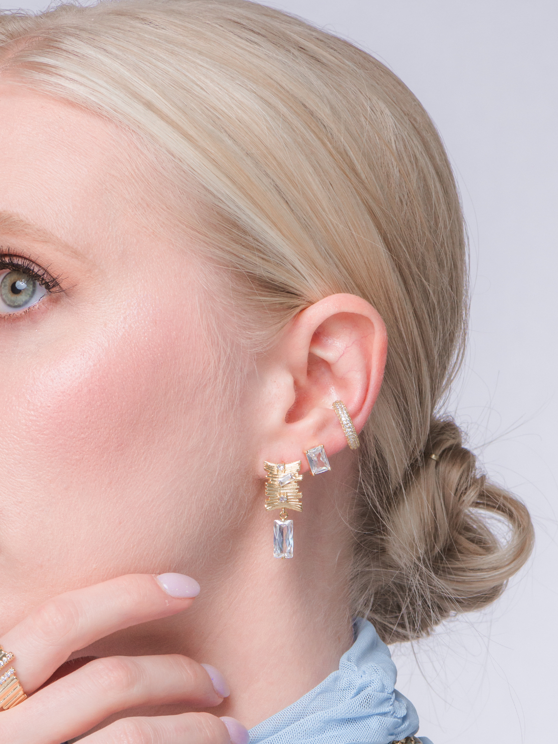 Close-up of a woman with blonde hair in a low bun, wearing multiple gold filled and gemstone earrings, including the 1.3" Zaza Earring by Kinsey Designs.