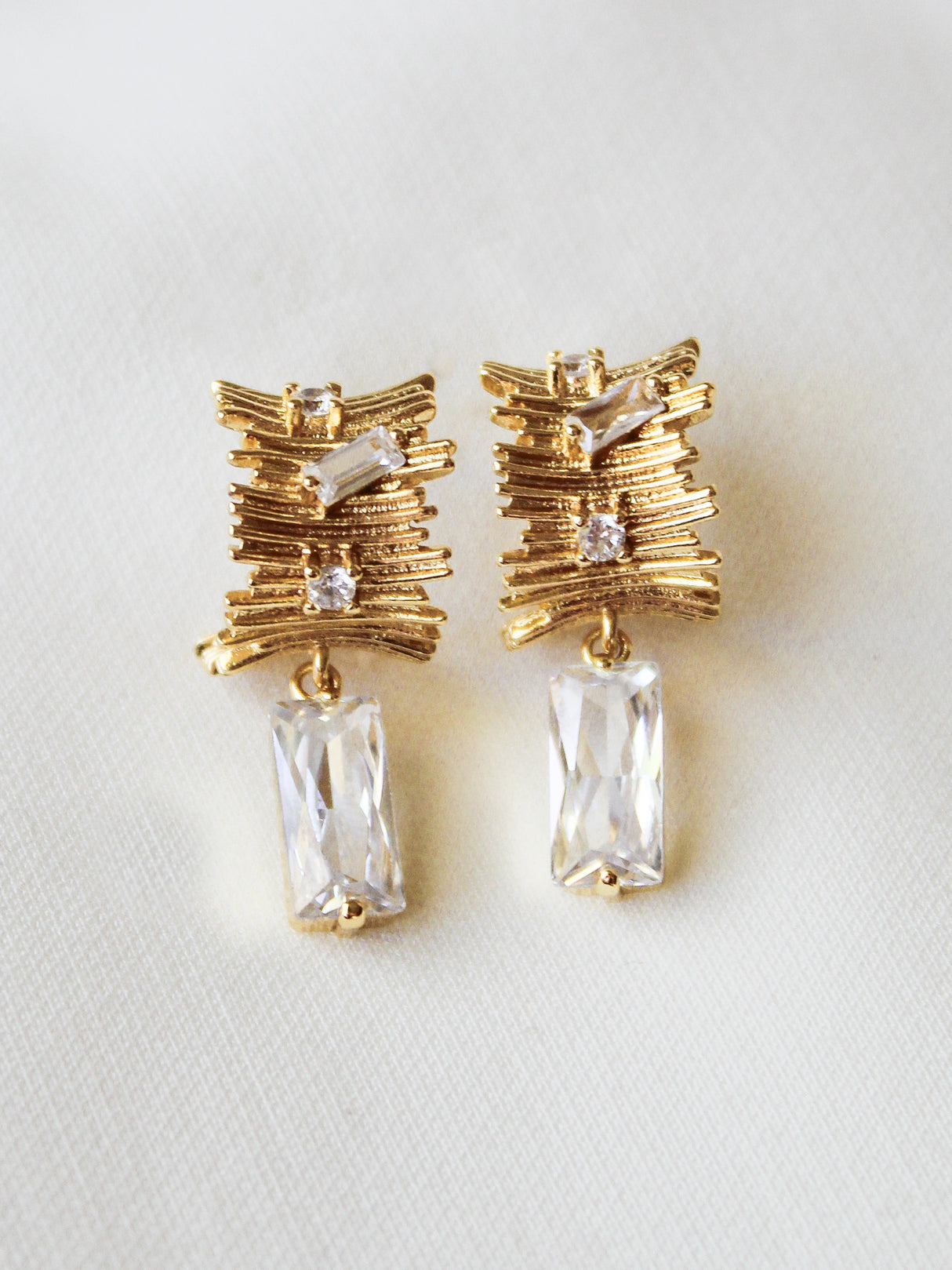 The Zaza Earring by Kinsey Designs is gold filled with a textured drop design, 1.3" long, featuring clear rectangular stones and small round crystals on a white background.