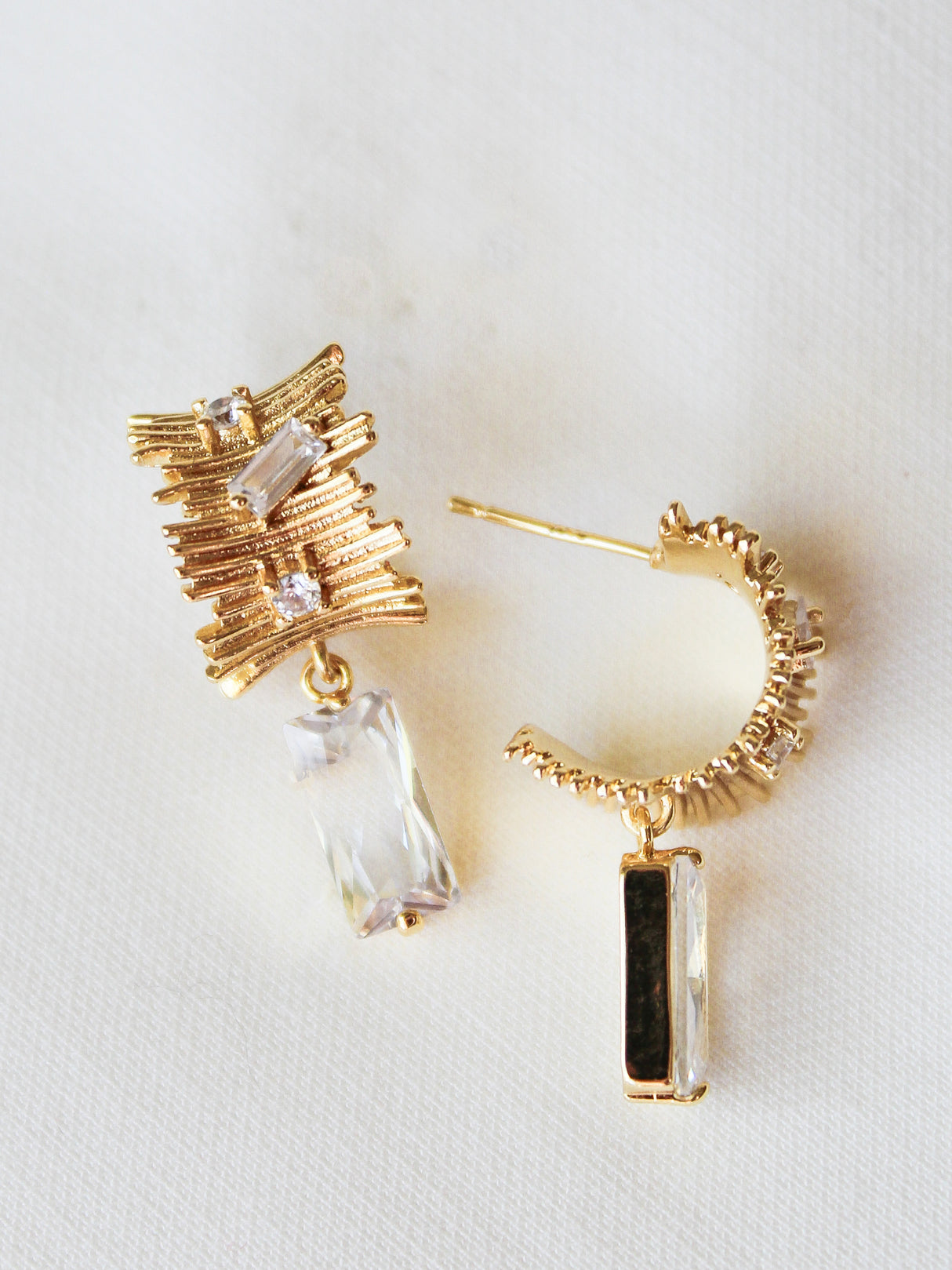 The Zaza Earring by Kinsey Designs features gold-filled, textured design with clear rectangular gemstones. Each earring is 1.3" long and shown on a white fabric background.