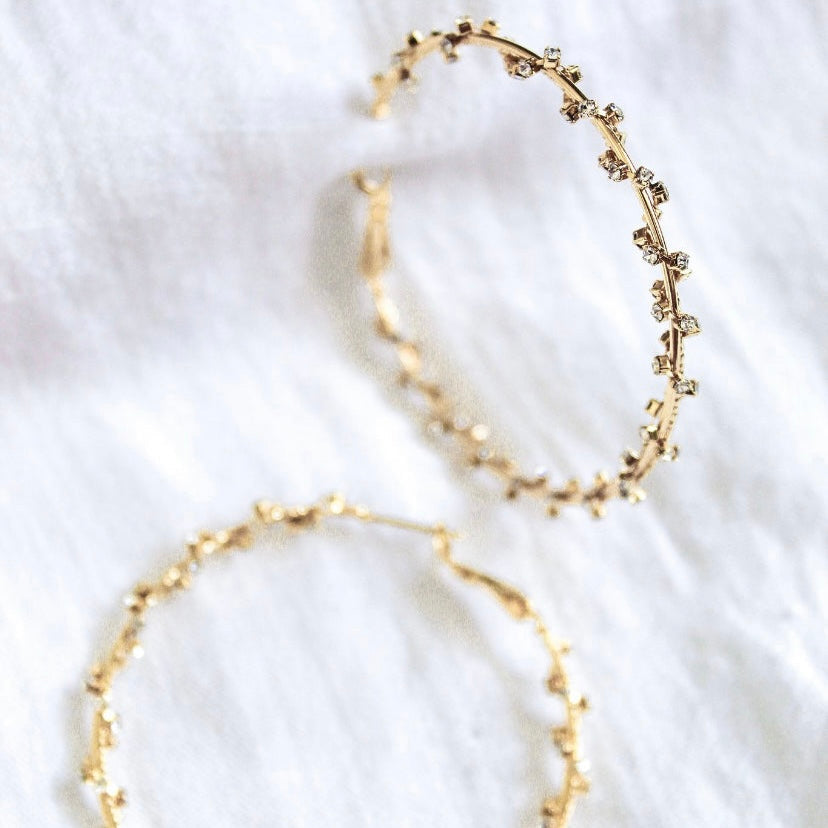 The Staci Hoop by Kinsey Designs Archives features gold plated hoops with sparkling cubic zirconia, 2" in diameter, shown on a white fabric background.