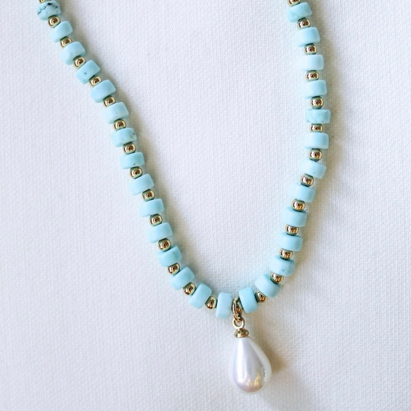 The Kinsey Designs Archives Sailor Pearl Necklace showcases light blue beads, gold accents, and a teardrop pearl pendant, forming a striking turquoise and gold set against a white background.