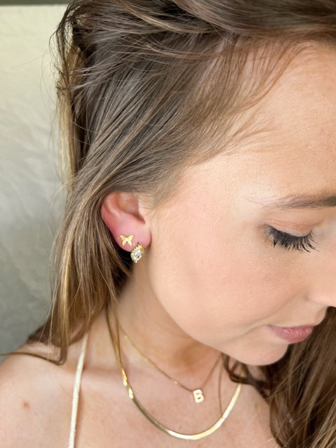 Woman with long brown hair wears Kinsey Designs Archives' Dina Post gold-filled butterfly and cubic zirconia stud earrings, paired with layered gold necklaces—must-have pieces you’ll love to find at a sample sale.