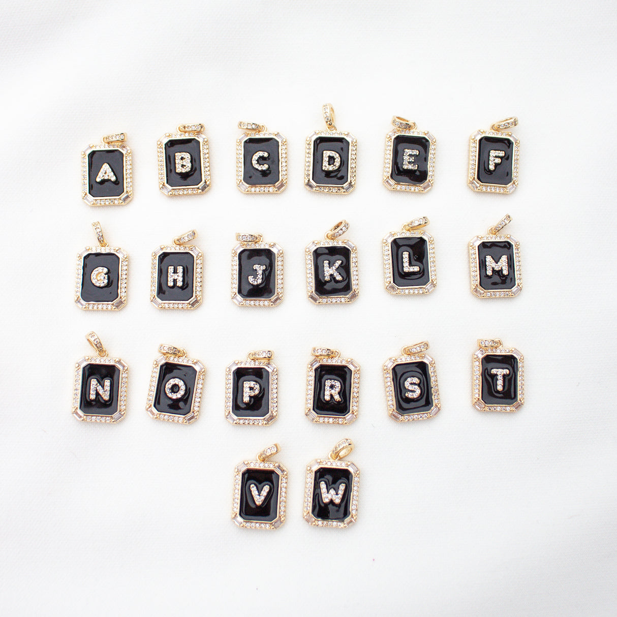 Kinsey Designs Archives' Initial Tile Necklace Ink Letter W features a gold-outlined black pendant with a white "W," displayed alphabetically with other letters on a white surface.
