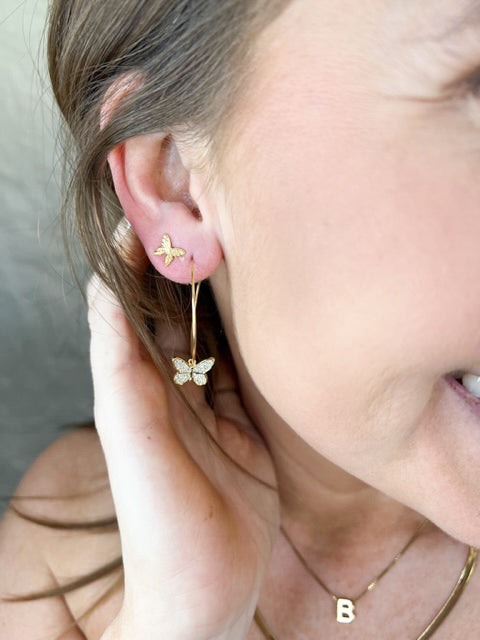 A woman wears Kinsey Designs Archives' Fleur gold plated butterfly earrings and a gold "B" letter pendant necklace, showcasing elegant jewelry.