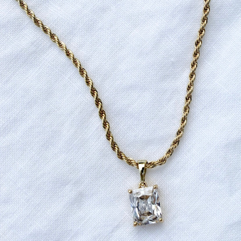 The Martin Necklace by Kinsey Designs Archives features a 19" twisted gold filled chain with a rectangular cubic zirconia pendant, elegantly displayed on a white fabric background.