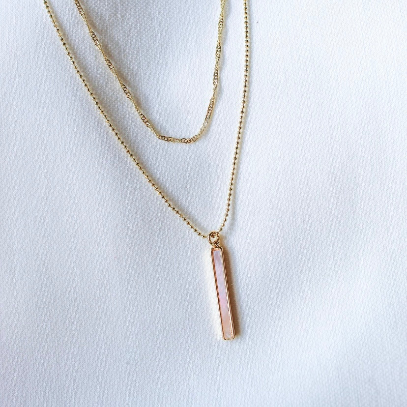 The Kalani Pearl Necklace by Kinsey Designs Archives, featuring a delicate gold-filled chain and a mother-of-pearl vertical rectangular pendant, is displayed on white fabric.