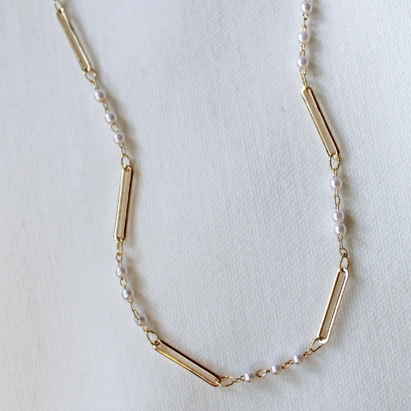 The Marina Pearl Necklace by Kinsey Designs showcases gold rectangular bars and small pearls, ideal for elegant pearl jewelry lovers, displayed on a light, textured background.