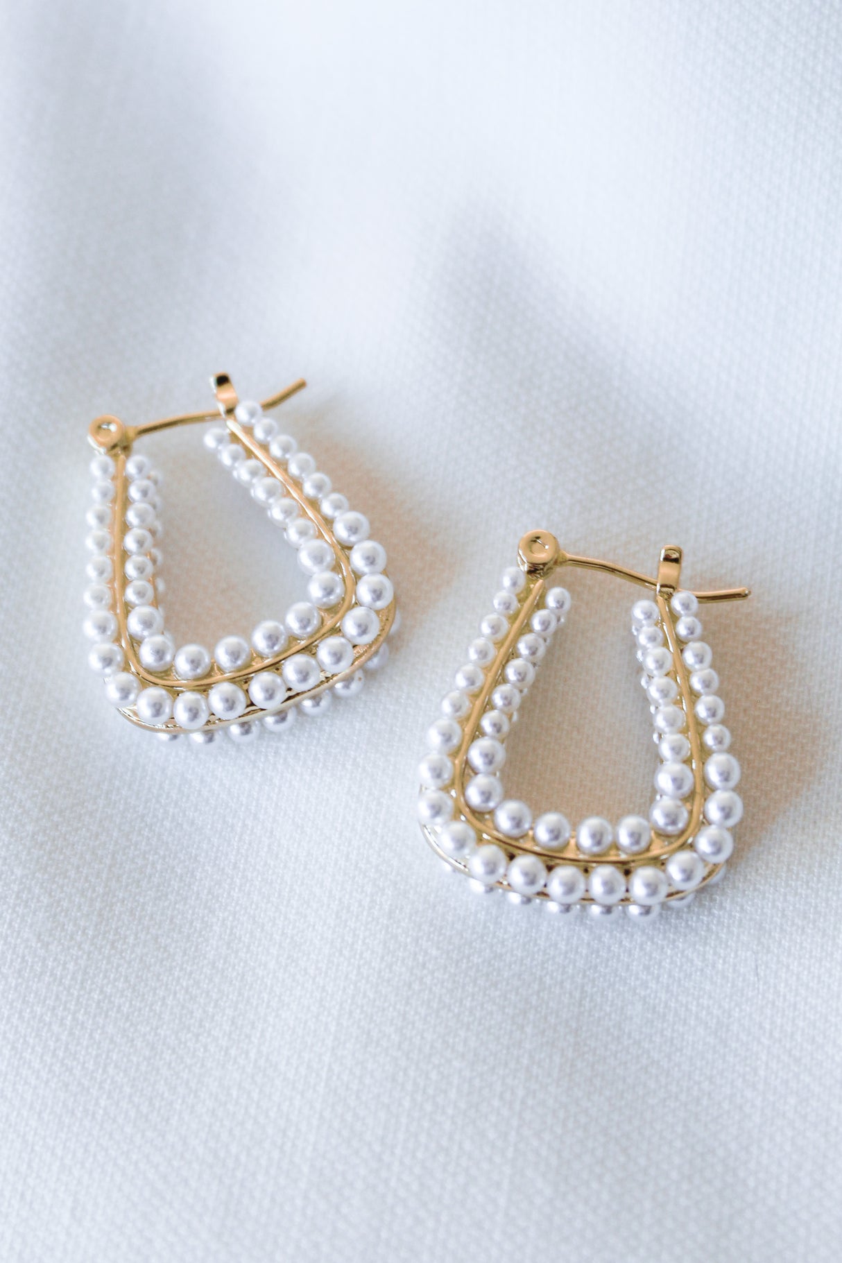 The Angla Hoop by Kinsey Designs Archives features 1" gold filled hoops adorned with two rows of small white pearls, displayed on white textured fabric.