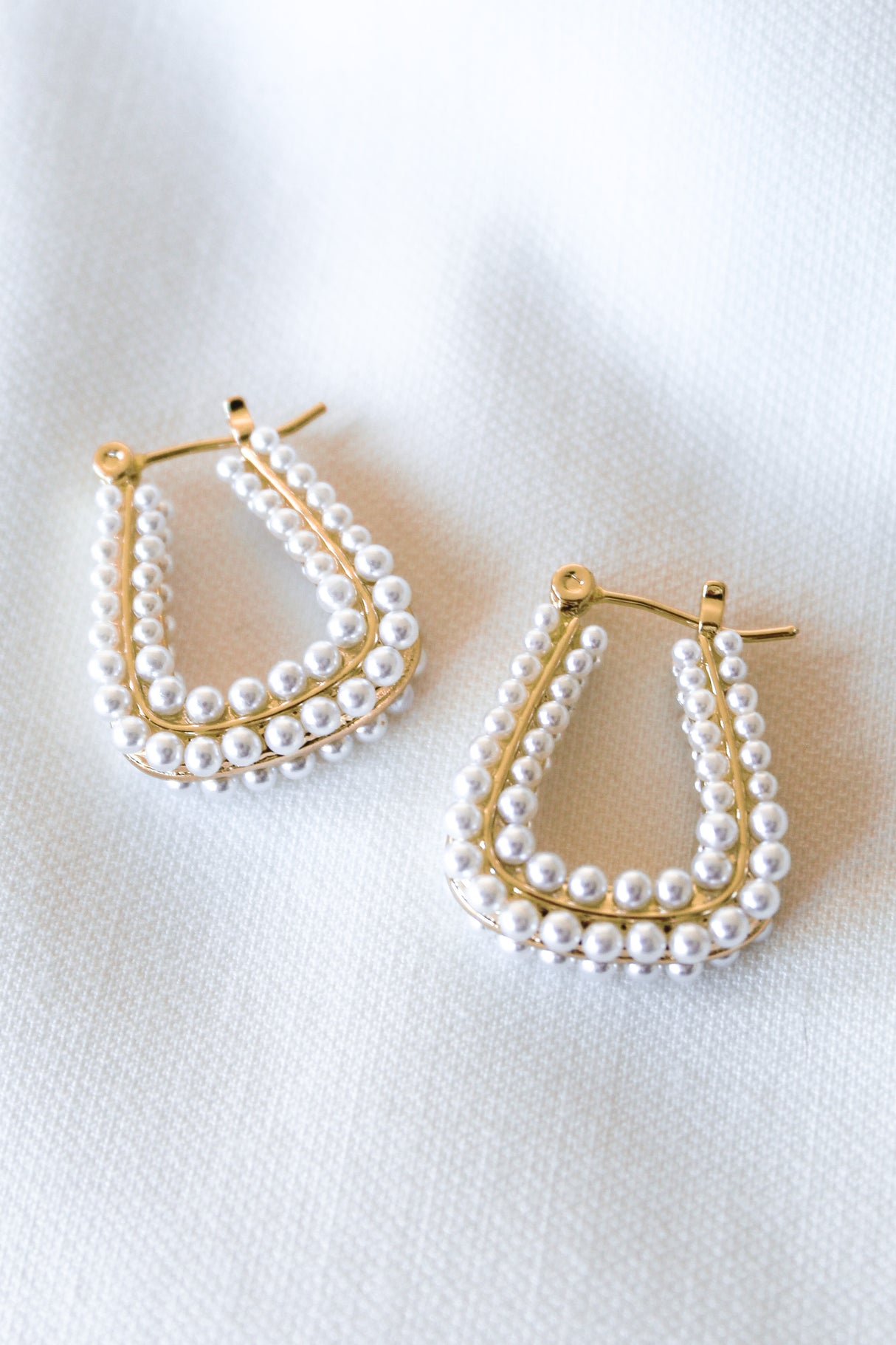 The Angla Hoop by Kinsey Designs Archives features gold-filled teardrop hoops with double rows of small white pearls, 1" in diameter, displayed on a light fabric background.