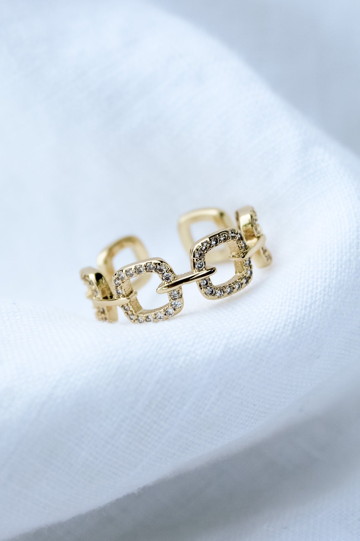 The Billie Ring by Kinsey Designs features gold-filled, square, diamond-studded links and is displayed on soft white fabric.