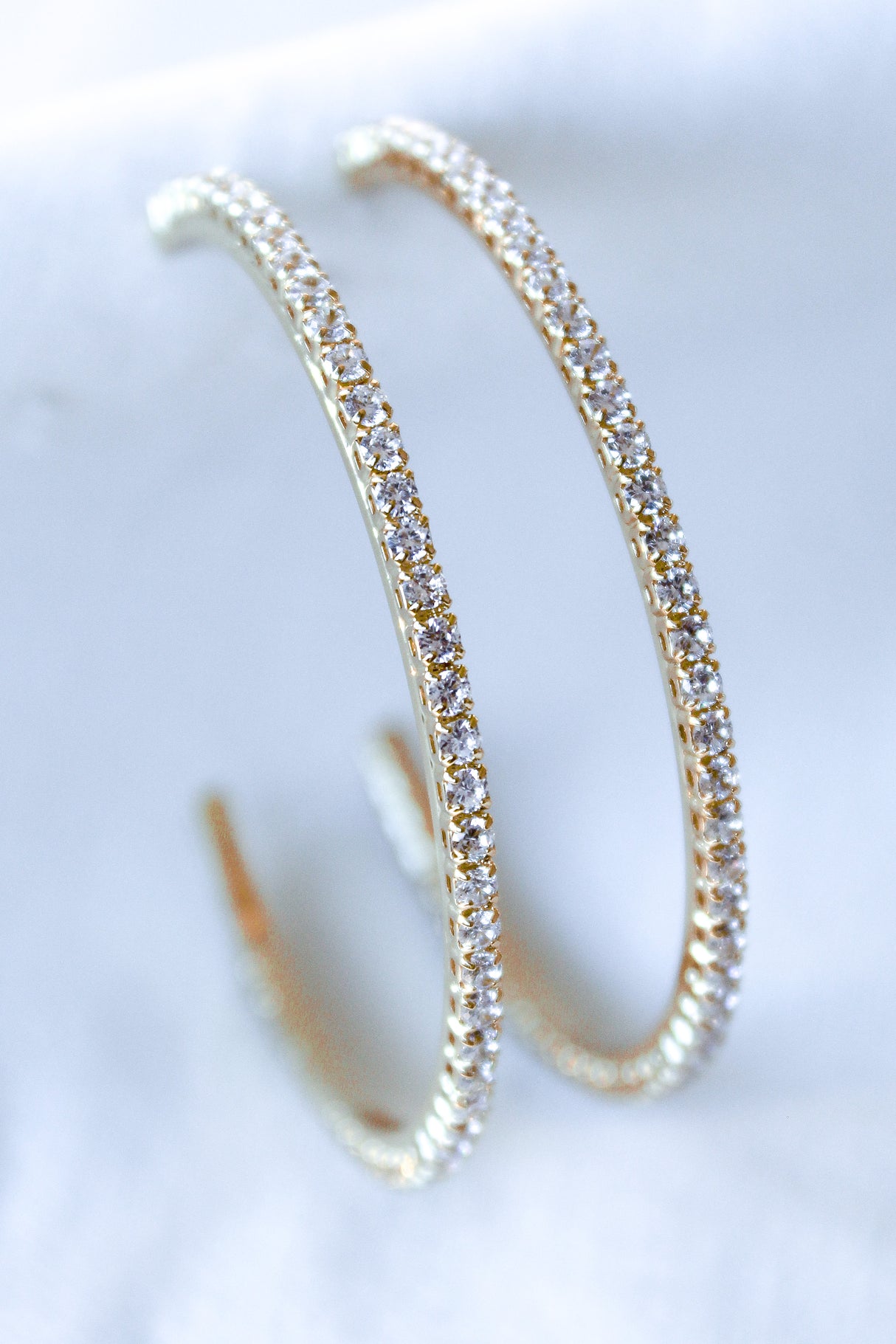 The Blaze Hoop by Kinsey Designs Archives features gold-filled hoops adorned with small cubic zirconia stones, showcased on a soft white surface.