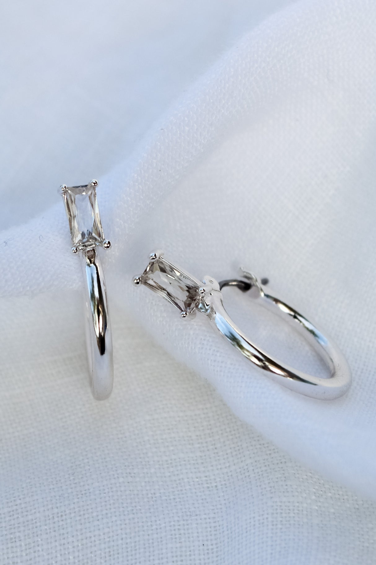The Darra Mini Silver hoop earrings by Kinsey Designs Archives feature rectangular Cubic Zirconia, crafted from rhodium-plated brass, measure 3/4" in diameter, and are elegantly displayed on white fabric.
