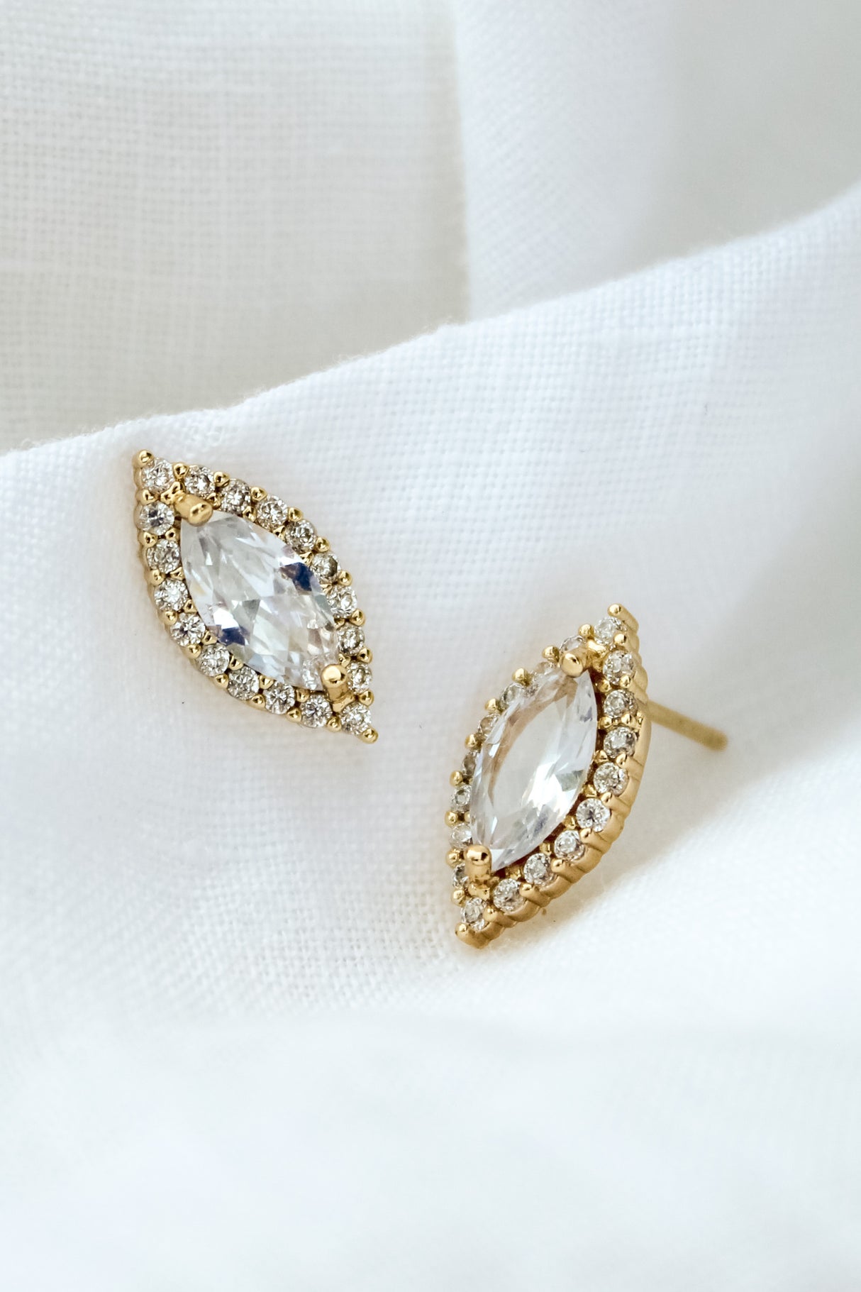 The Dina Post by Kinsey Designs Archives features gold filled marquise-shaped stud earrings with cubic zirconia and a halo of small diamonds, beautifully displayed on white fabric.