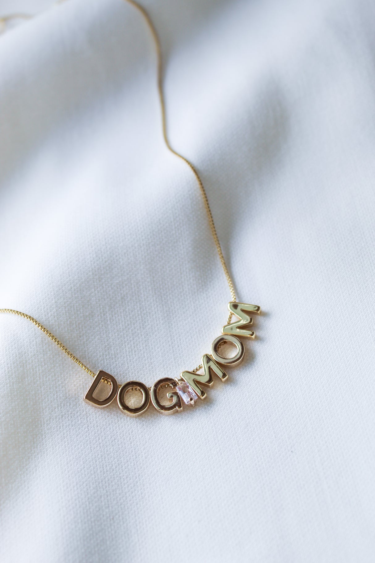 Dog Mom Slide Necklace by Kinsey Designs Archives shown on white fabric, featuring “DOG MOM” gold letter charms on an 18" gold filled chain with adjustable Italian closure.