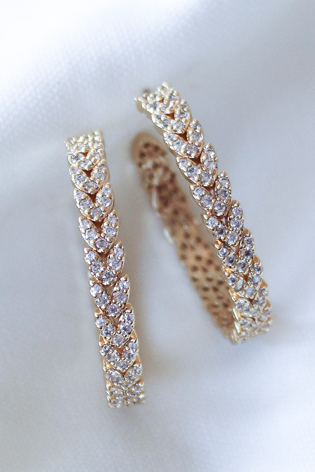 The Dottie Heart Hoop by Kinsey Designs Archives features a leaf pattern with sparkling cubic zirconia, showcased on a white fabric background.