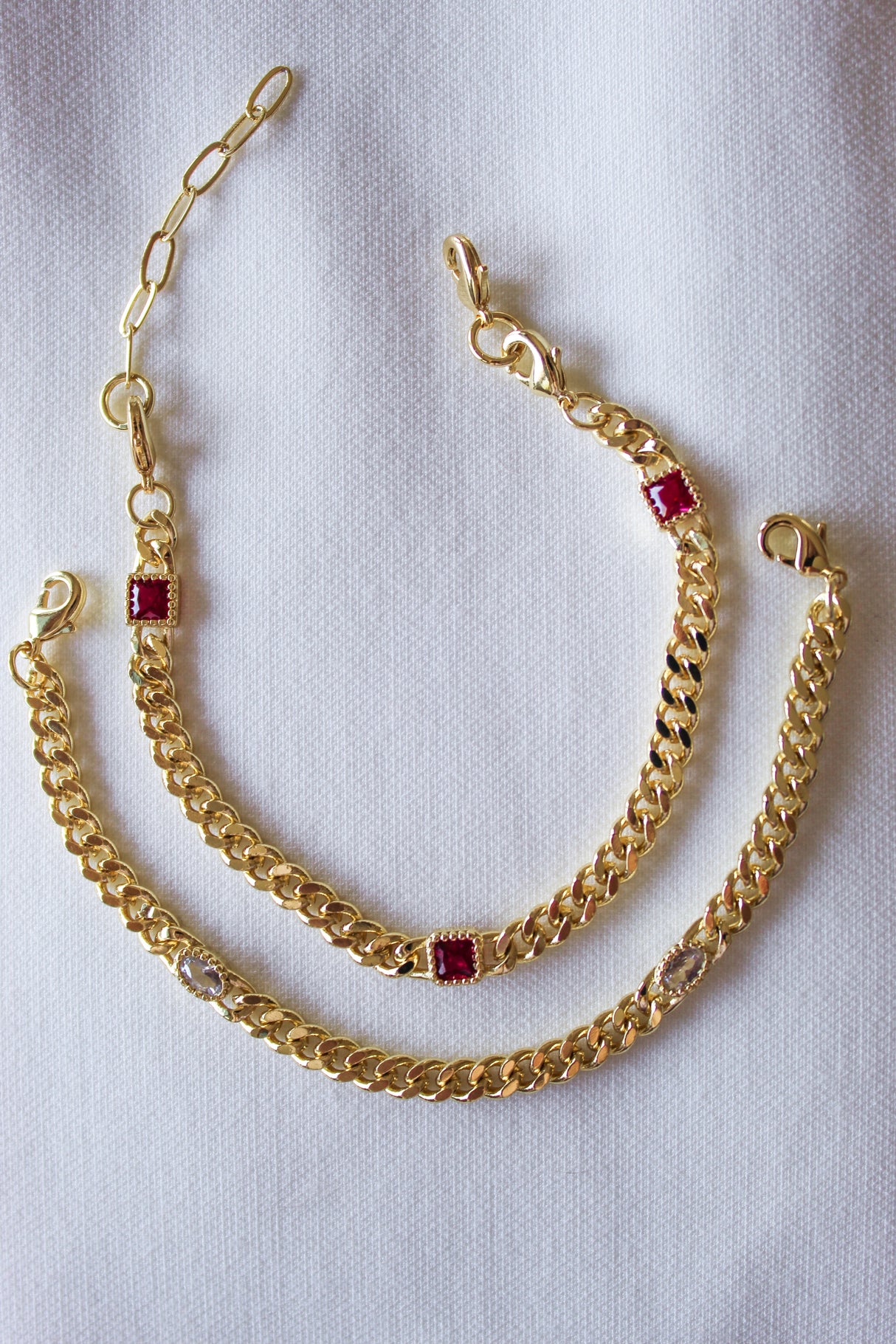 The Kinsey Designs Dublin Bracelet (3 in 1), featuring gold-filled chains with gemstone and cubic zirconia accents, rests on a white fabric background.