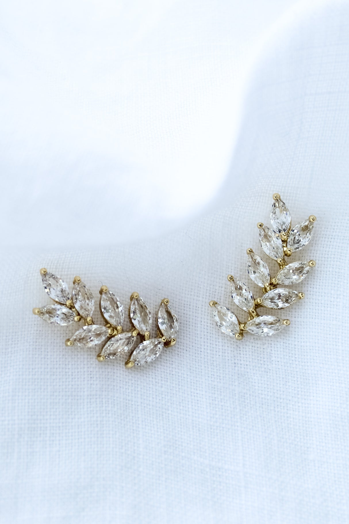 The Elio Climber by Kinsey Designs Archives features leaf-shaped clear gemstones in a curved design—chic earrings perfect for a stylish sample sale find, beautifully displayed on white fabric.
