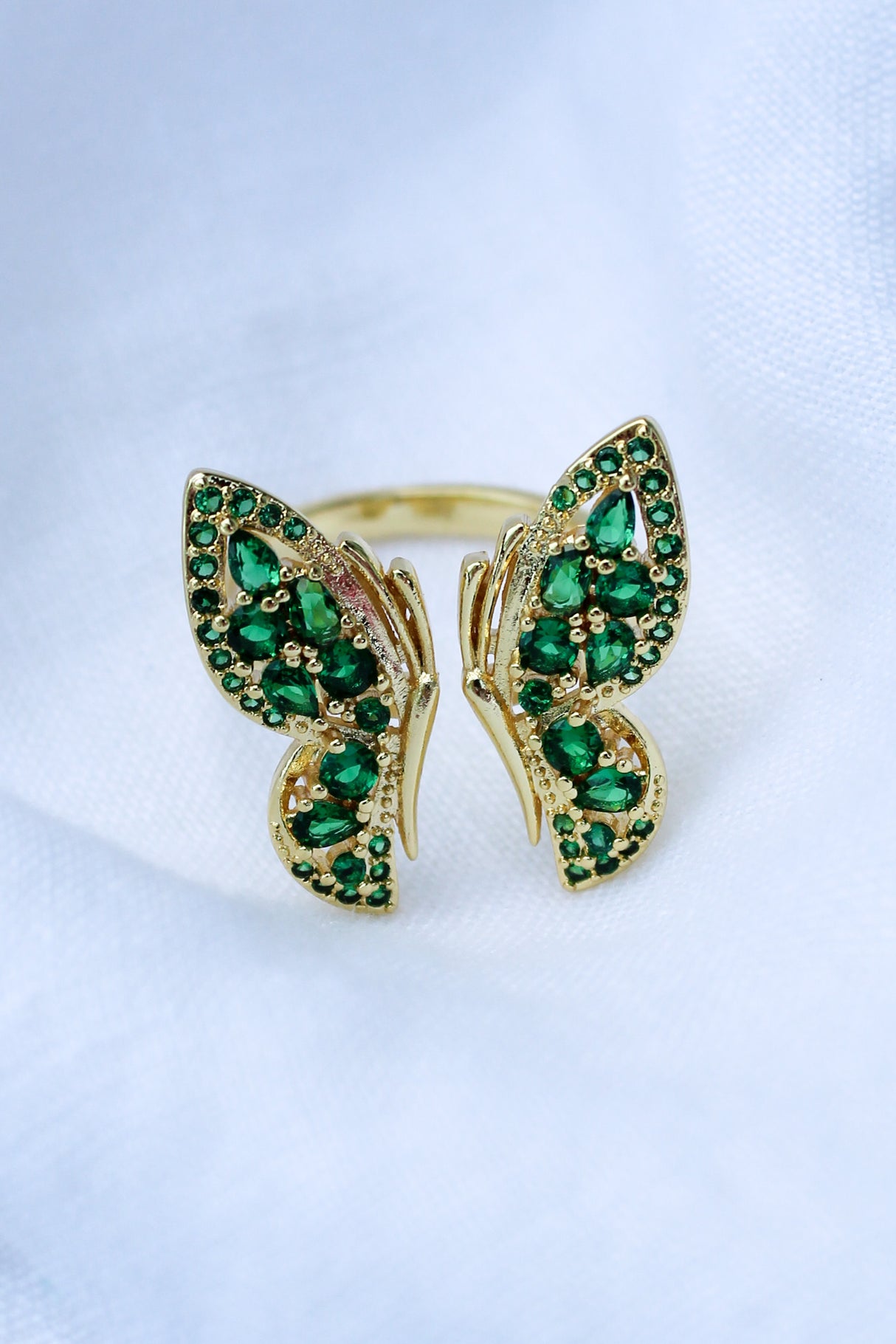 The Ezra Ring by Kinsey Designs Archives features a gold-filled butterfly shape with a .75" face, set with green gemstones and shown on a white fabric background.