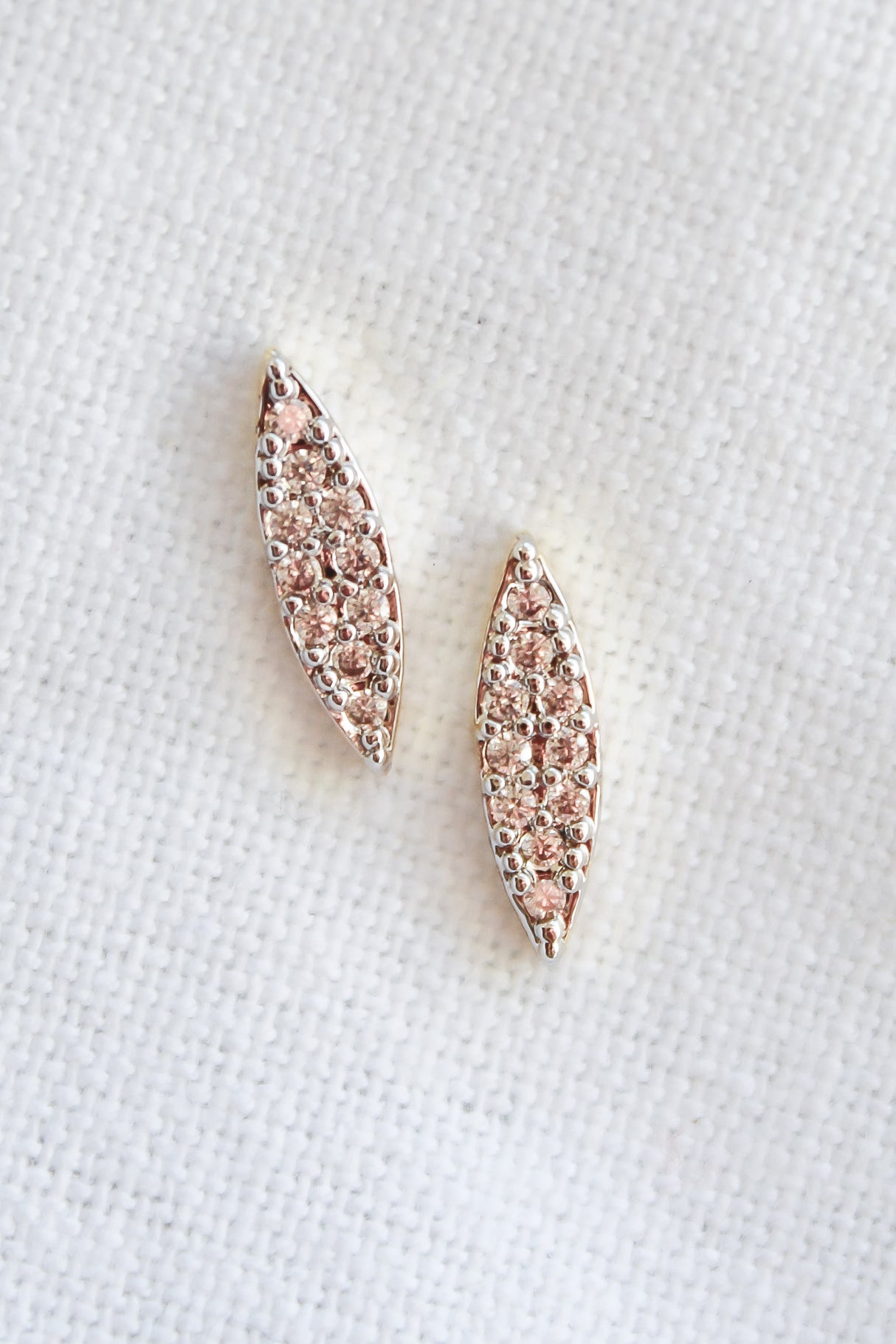 The Her Post earrings by Kinsey Designs Archives feature two marquise-shaped, 16k rose gold filled pieces adorned with sparkling cubic zirconia, displayed on a white textured background.