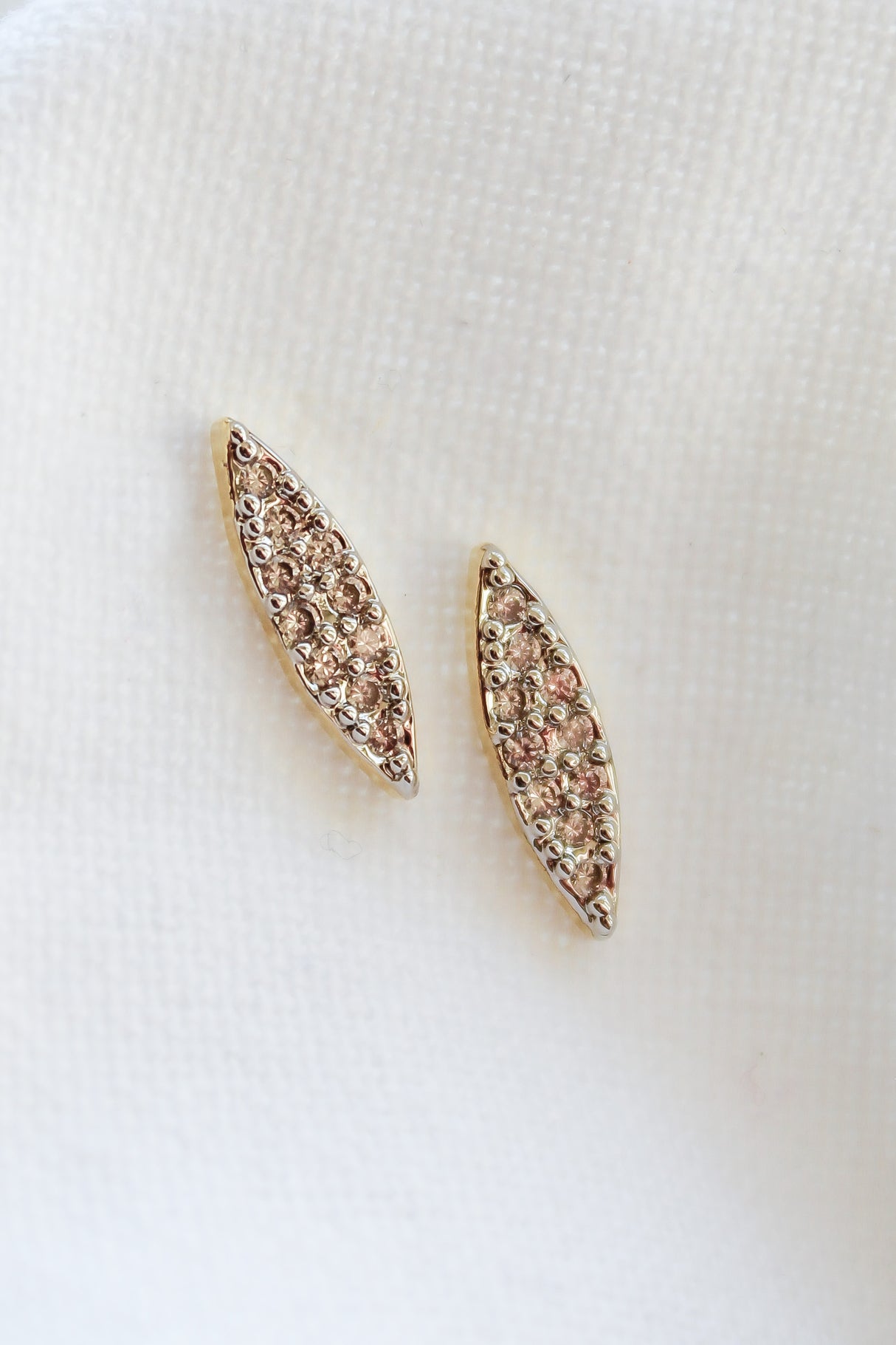 Her Post earrings by Kinsey Designs Archives feature a marquise shape, 0.5" wide, crafted in 16k gold filled metal with sparkling cubic zirconia accents. Shown on a white textured fabric background.