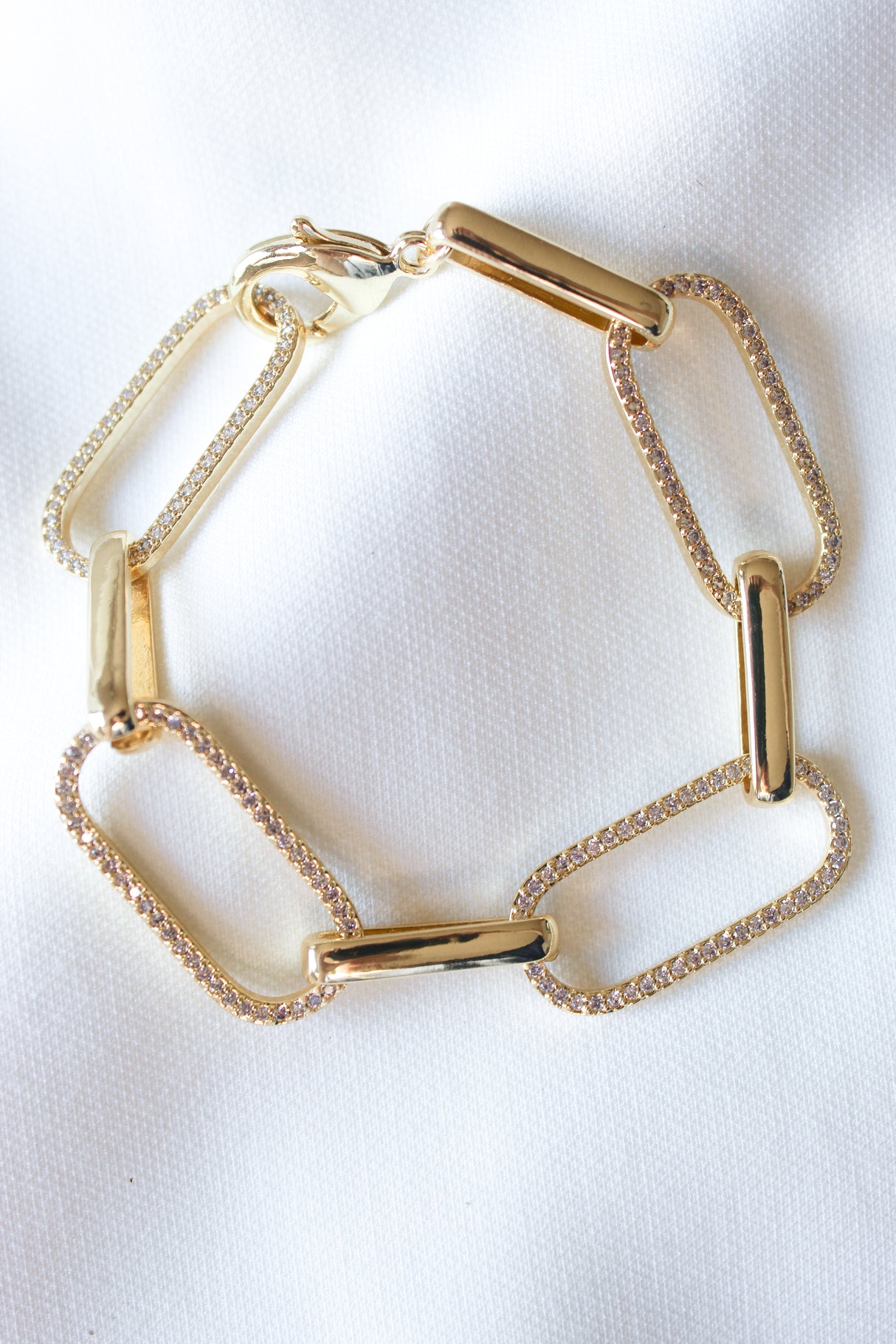 The Kinsey Designs Jameson Bracelet features rectangular gold filled links, some adorned with sparkling cubic zirconia, shown on a white fabric background.