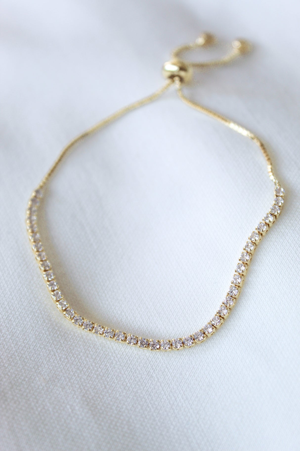 The Katie Bracelet by Kinsey Designs features gold-filled links and sparkling cubic zirconia, elegantly displayed on a white fabric background.