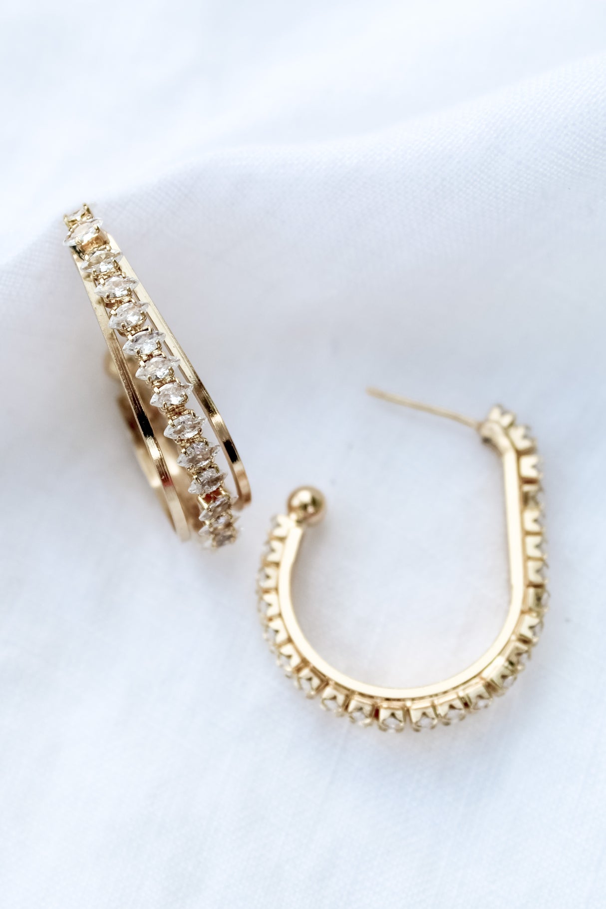 The Kenny Earring by Kinsey Designs Archives features gold-filled hoops with embedded cubic zirconia, adding subtle sparkle to your jewelry collection. Shown against a white fabric background.