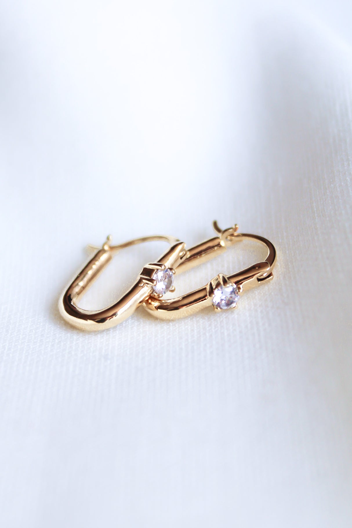 The Lou Hoop by Kinsey Designs Archives features 14k gold plating and small round cubic zirconia stones, displayed on a soft white fabric background.
