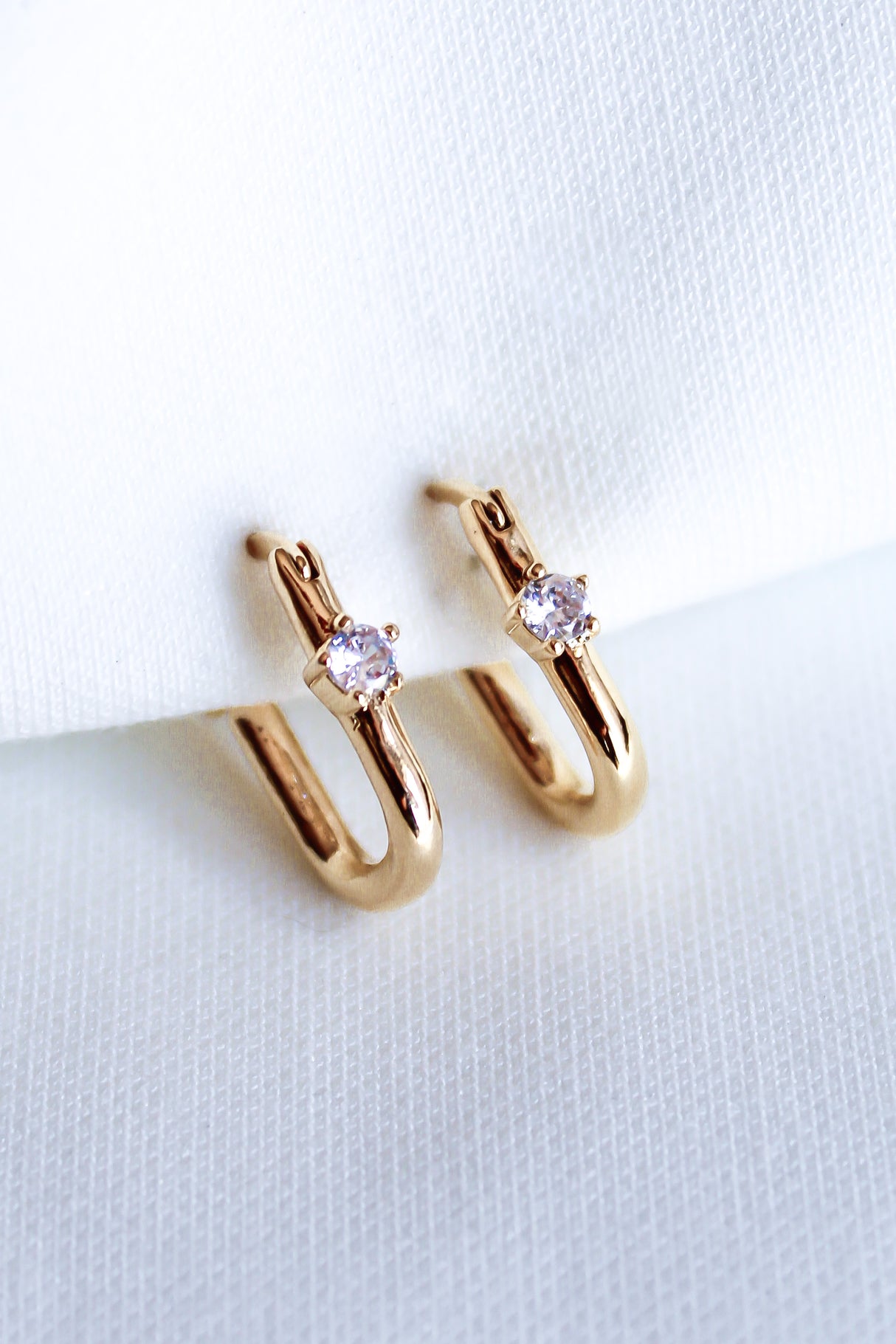 The Lou Hoop by Kinsey Designs Archives features 14k gold plating and small clear cubic zirconia stones, elegantly presented on white fabric.