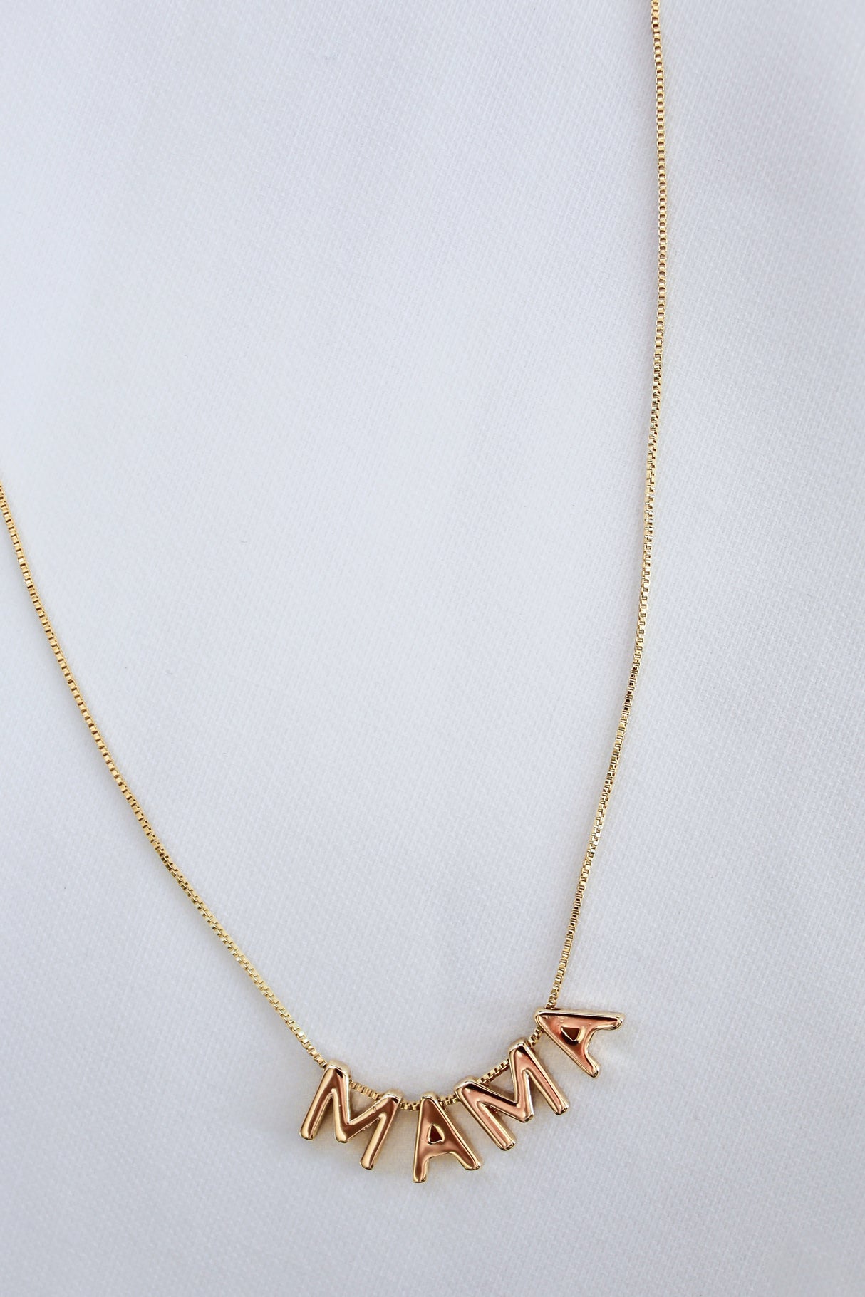 The MAMA Slide Necklace by Kinsey Designs Archives features letter charms spelling "MAMA" on a white fabric, an 18" chain, adjustable Italian closure, and radiant 14k gold filled finish.