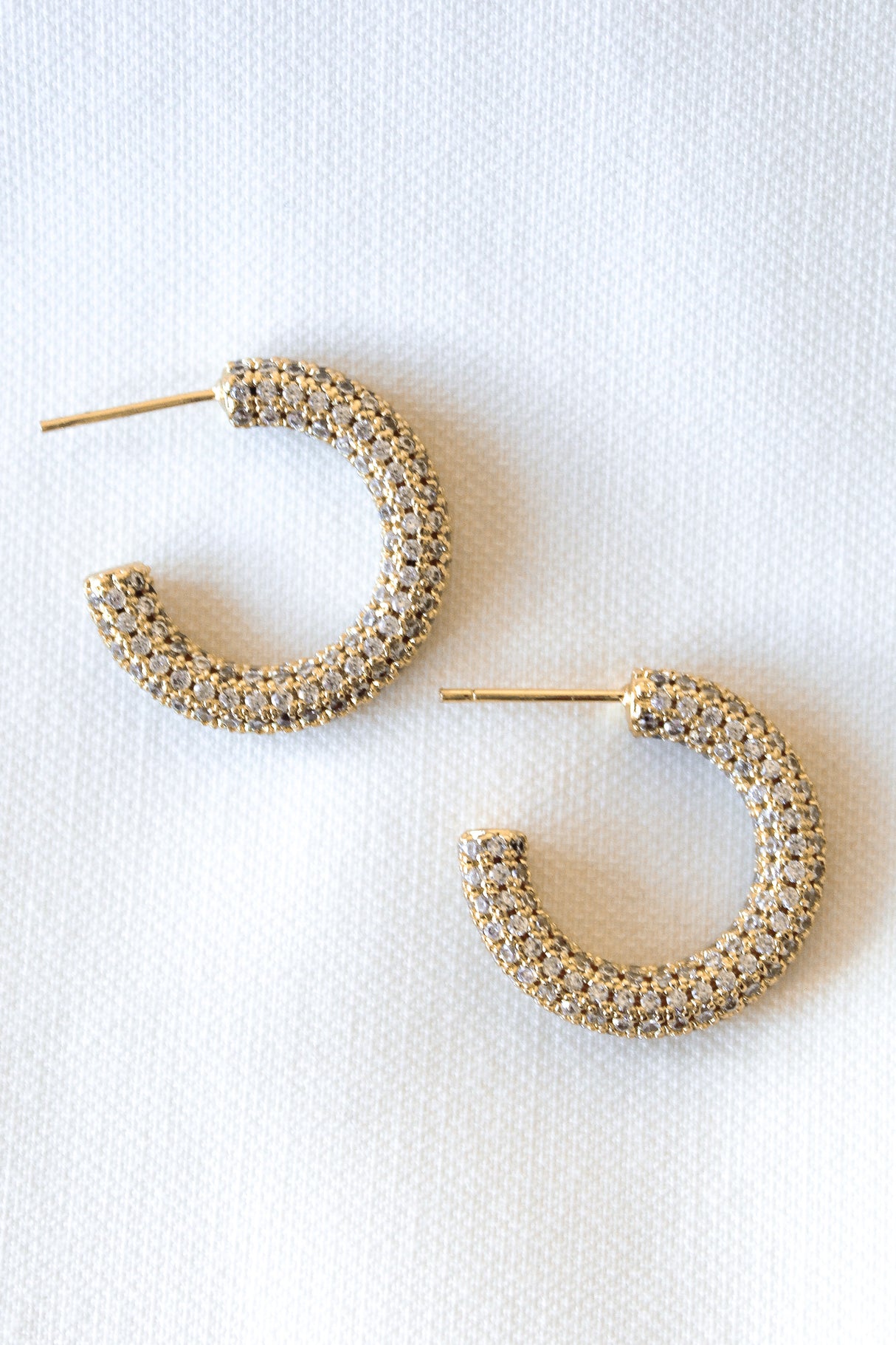 The Melli Hoop by Kinsey Designs features a gold filled, woven-texture design. Displayed on a white fabric background, these hoops add elegance to any look—now available in our Sample Sale!.